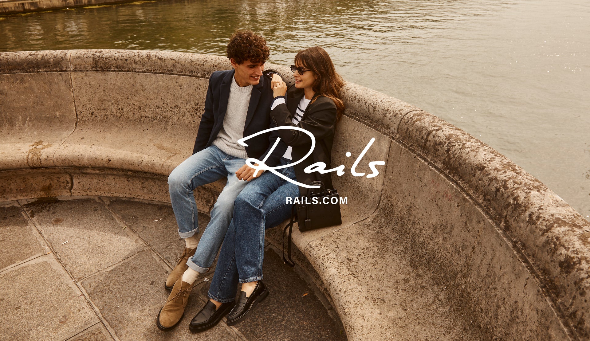 EDITORIAL IMAGE OF TWO MODELS SITTING OUTSIDE. FIRST MODEL IS WEARING LARK COAT, DONOVAN SWEATER, AND CLAYTON SLIM STRAIGHT JEANS. SECOND MODEL IS WEARING JAC BLAZER, GEMMA SWEATER, AND TOPANGA STRAIGHT JEANS.