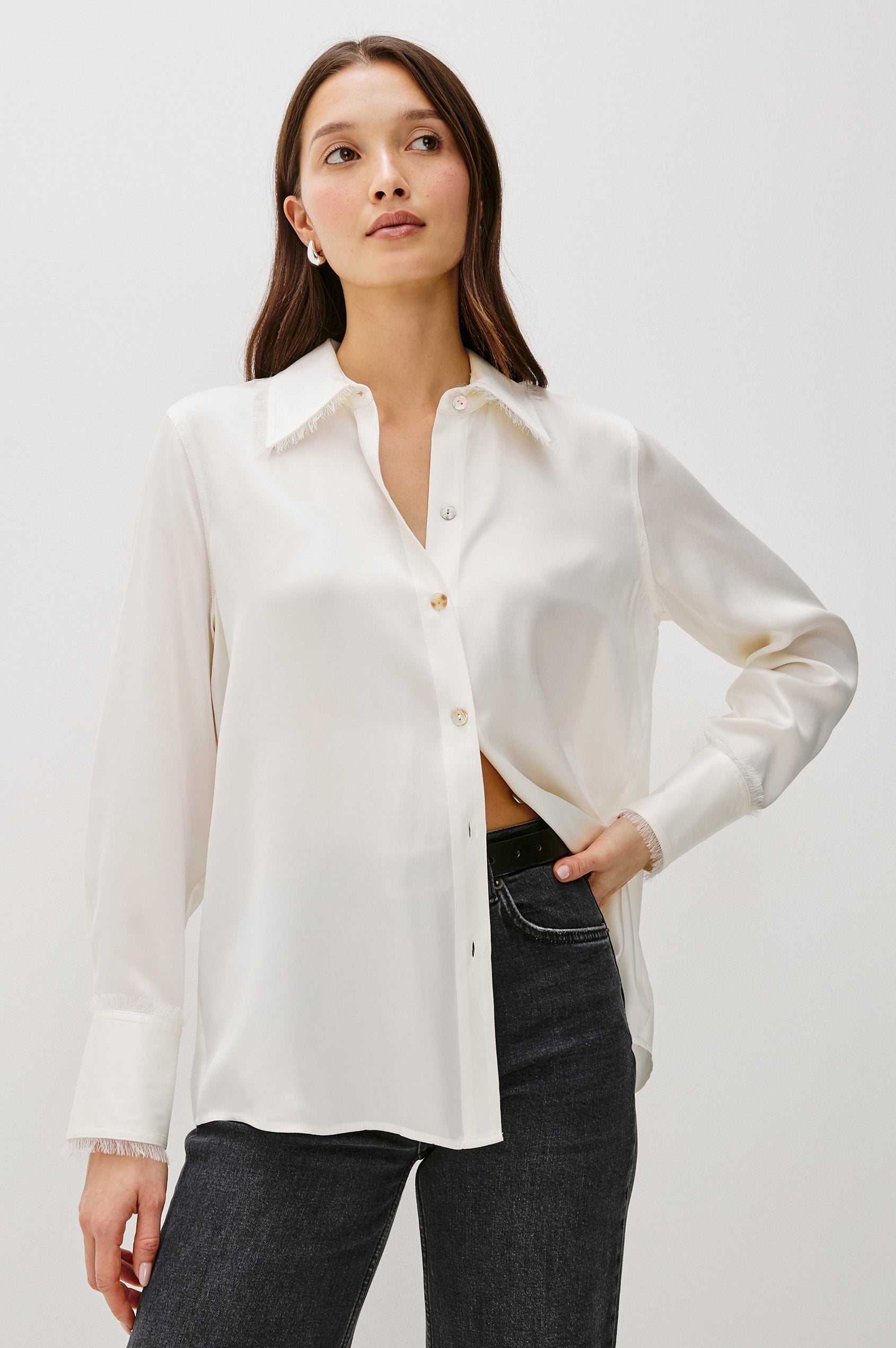 Abbey silk long sleeve button-down shirt with a raw edge trim at the collar and sleeve cuffs in Ivory colorway - front view on model with hand on waist