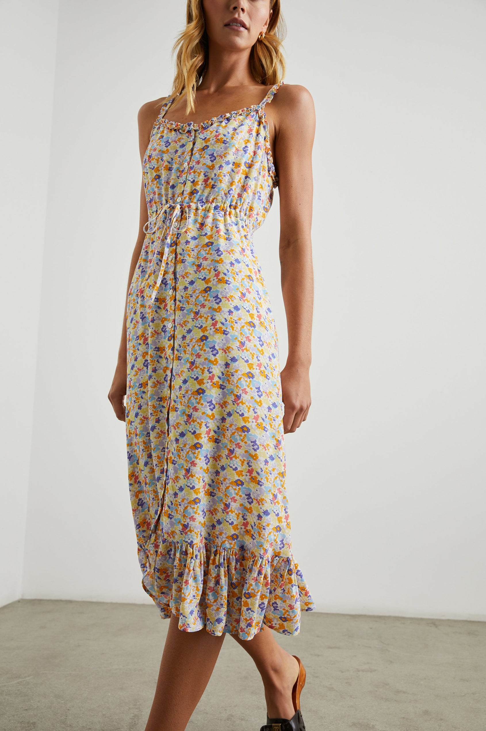 Adalyn Sleeveless Midi Dress with Thin Shoulder Straps, Buttons Down the Front, a Drawstring Waist, a Ruffled Hem and Ruffled Trim in Papaya Flowers Colorway, Purples, Blue, Yellow and Orange on White - Front Full Body View Featured on Model 