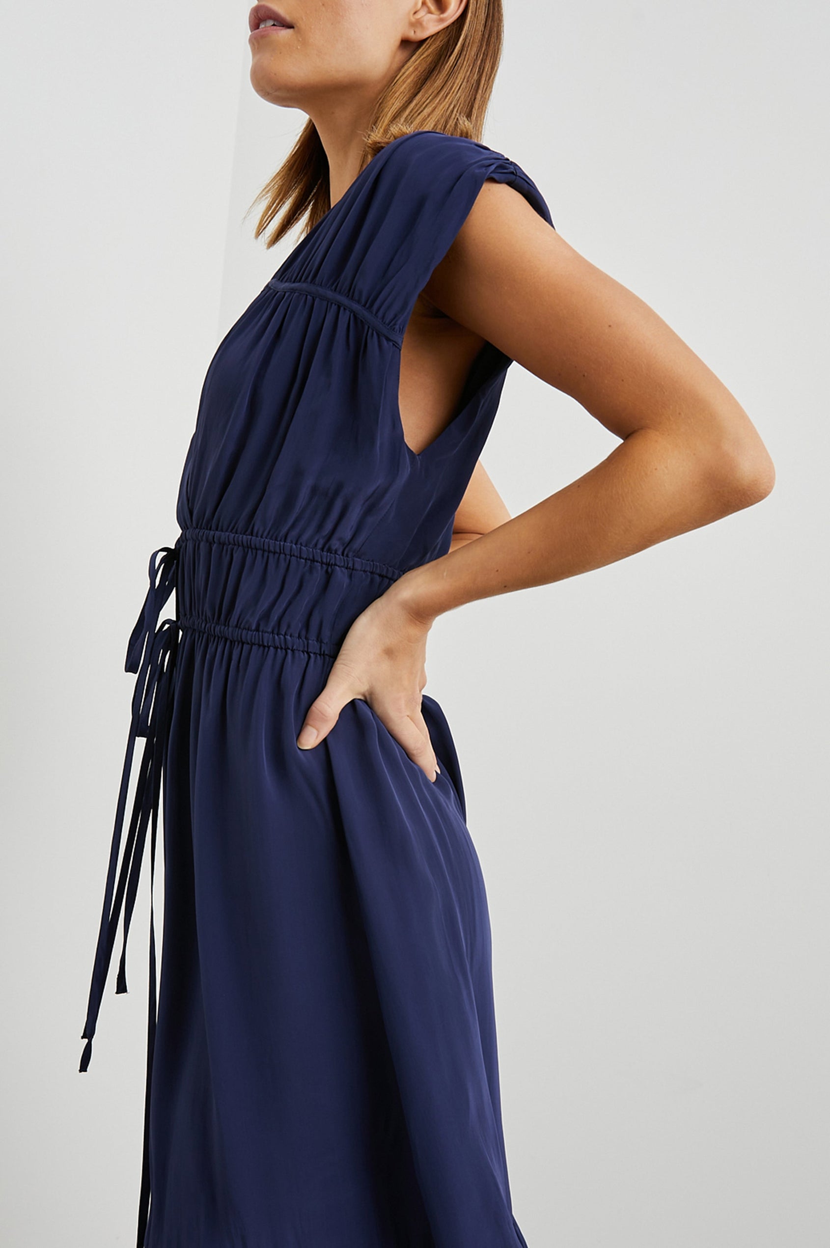 Aletta Short Sleeve Midi Dress with Cap Sleeves with Wide Arm Holes, Two Drawstrings at the Waist, a Deep V Neck, a Tiered Skirt and Ruching at the Front Yoke Seam and Shoulder Seam in Admiral Blue Colorway - Side View Featured on Model 
