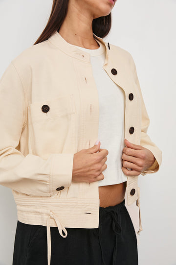 Alma Jacket with Button Closure, Mandarin Collar, Two Large Chest Button Patch Pockets and a Drawcord at the Hem in Ecru Colorway, with Dark Buttons - Front View Featured on Model