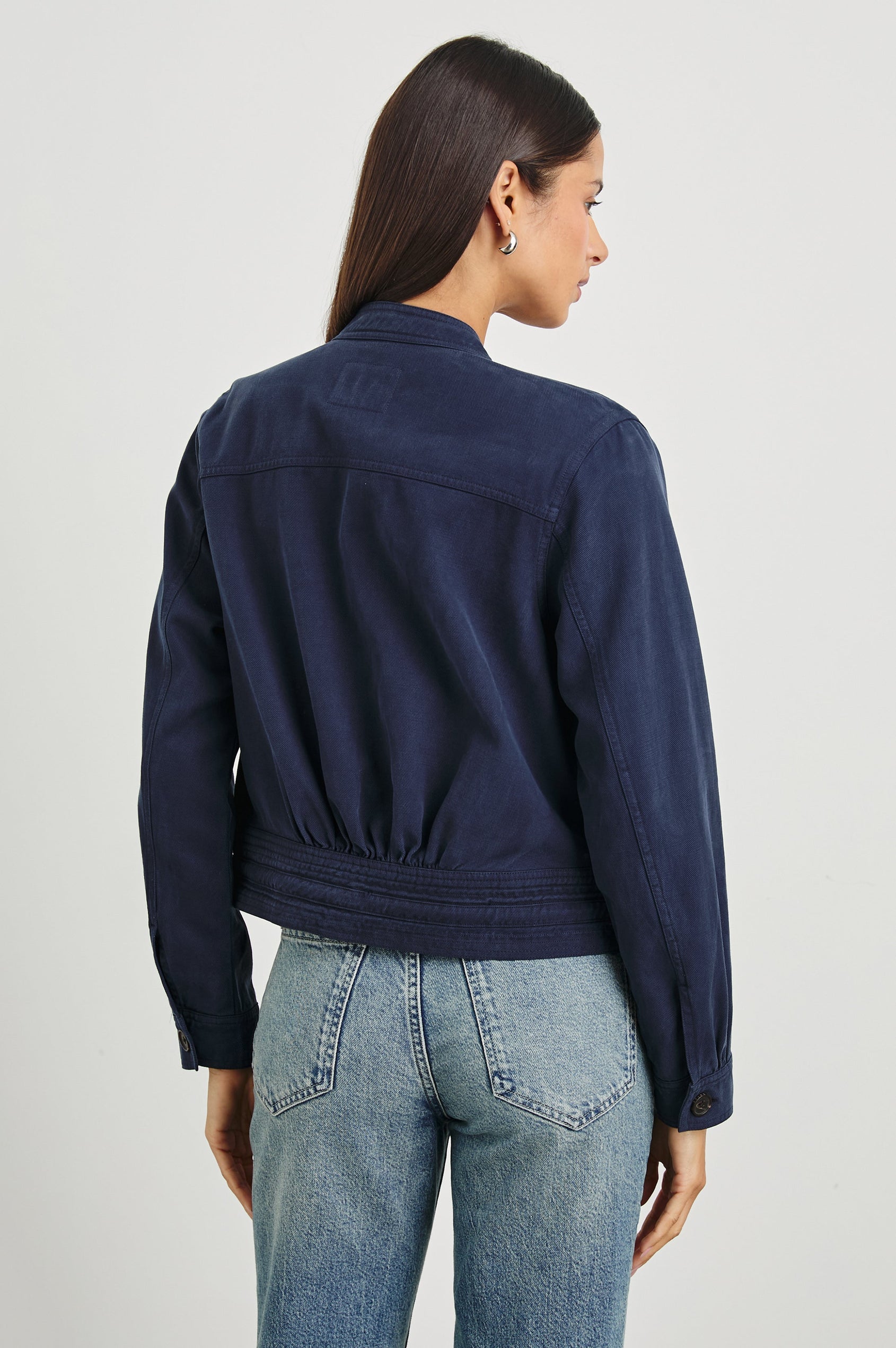 Alma Jacket with Button Closure, Mandarin Collar, Two Large Chest Button Patch Pockets and a Drawcord at the Hem in Navy Colorway - Back View Featured on Model