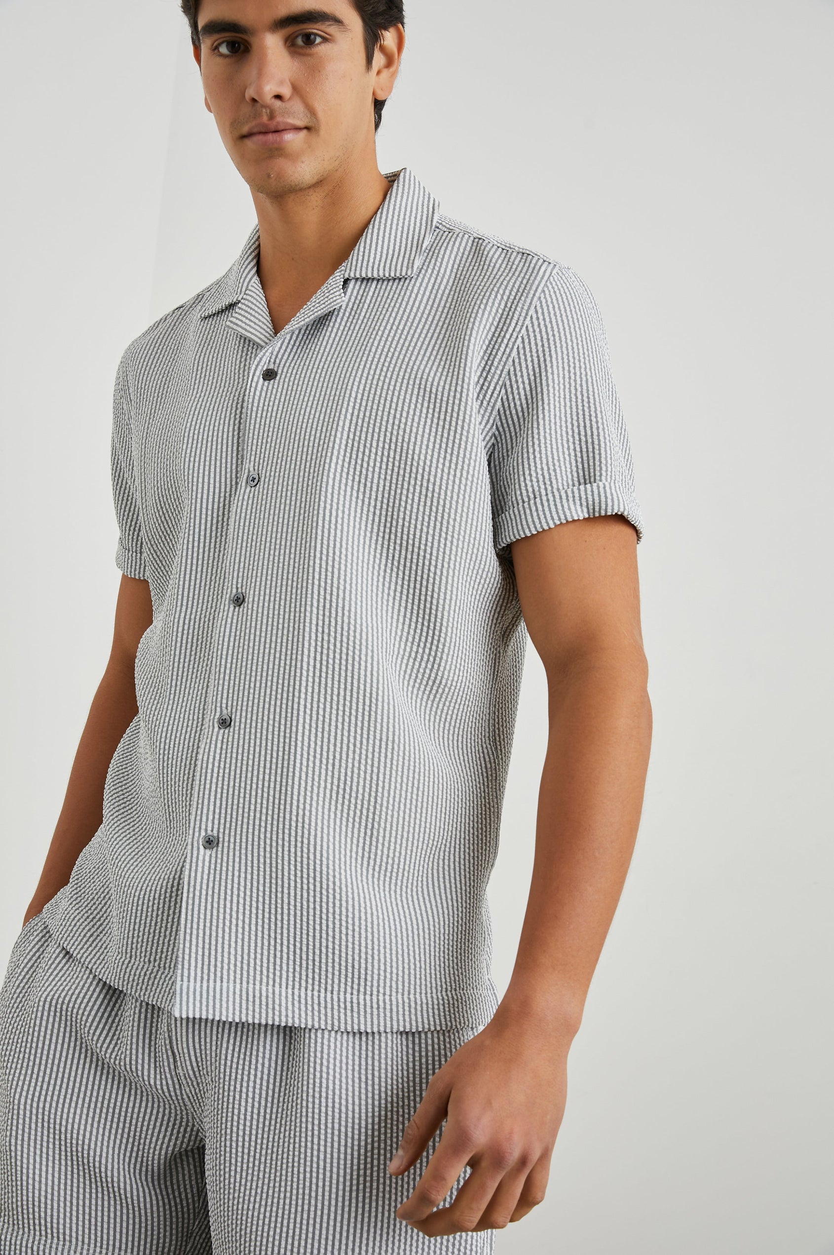 Amalfi Short-Sleeve Button Up in Faded Seersucker Colorway, Grey and white thin vertical stripes  - Front View Featured on Model