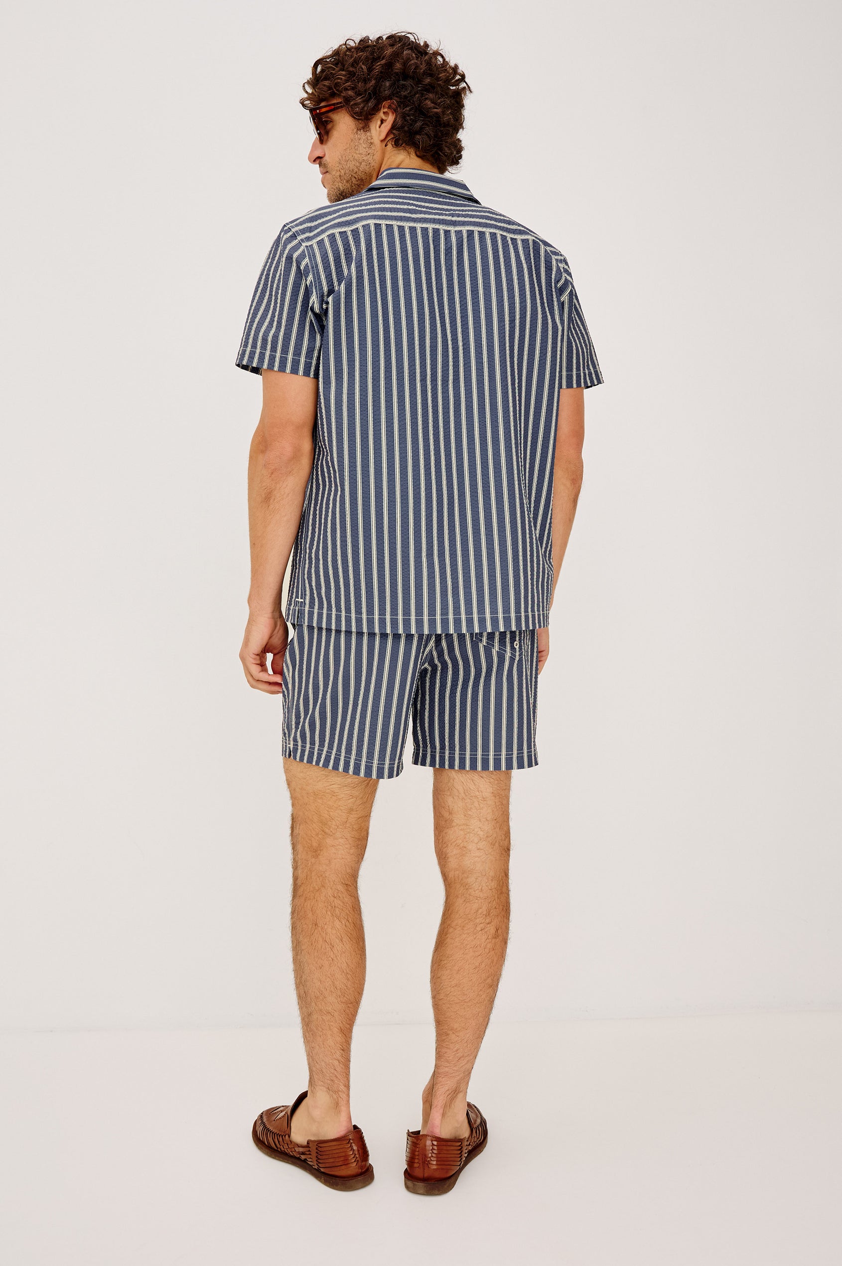 Amalfi Camp Shirt in Lightweight Seersucker With Notched Collar, Front Buttons, Short Sleeves, and Relaxed Fit in Navy Cream Stripe Colorway - Full Body Back View Featured on Model