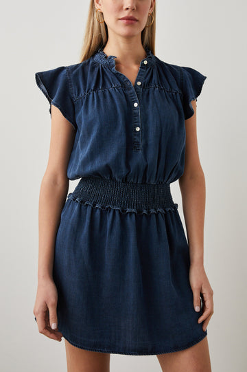 Amina Short Sleeve Denim Mini Dress with Flutter Sleeves, a Ruffled Collar, a Button Placket, and a Shirred Waist in Dark Vintage Colorway - Front View Featured on Model 
