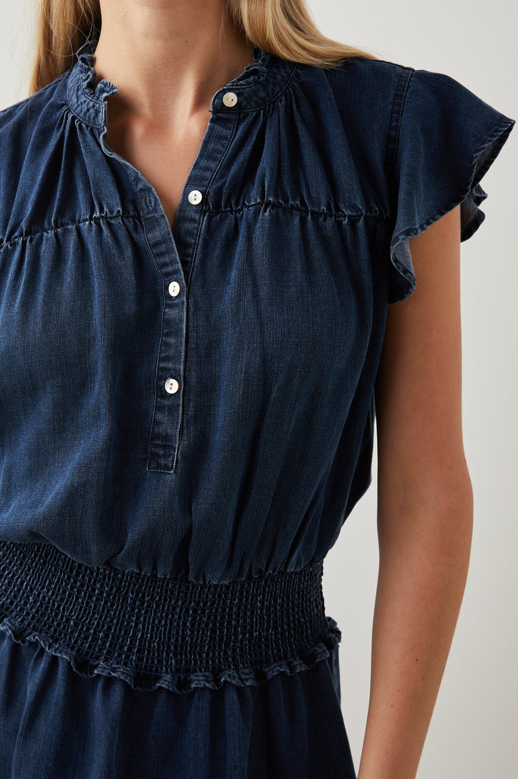 Amina Short Sleeve Denim Mini Dress with Flutter Sleeves, a Ruffled Collar, a Button Placket, and a Shirred Waist in Dark Vintage Colorway - Front View Featured on Model 