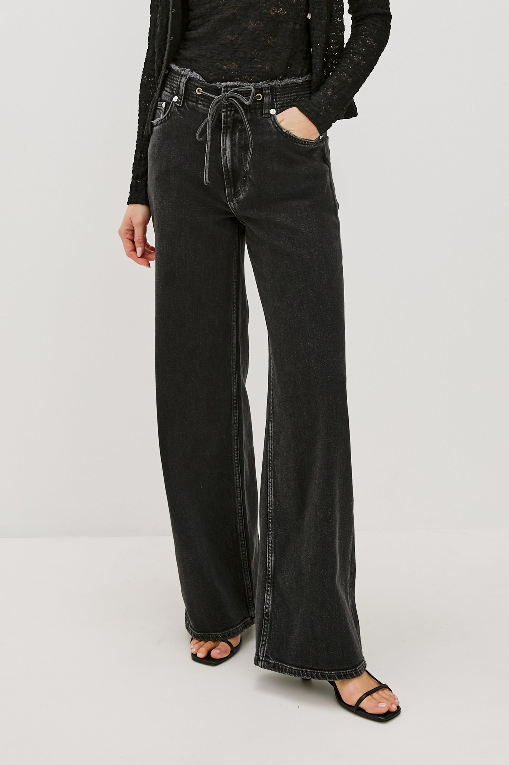 Angeleno mid rise slouchy wide leg jean with a drawstring waist tie, gromets and a raw edge waistband in a black wash Ash Black - front view featured on model.