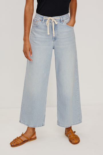 Angeleno Crop Denim Pant, Wide Leg, Five Pocket Zip Fly with a White Drawstring Tie at Waist in Light Wash Scuba Colorway. Front View Shown on Model.