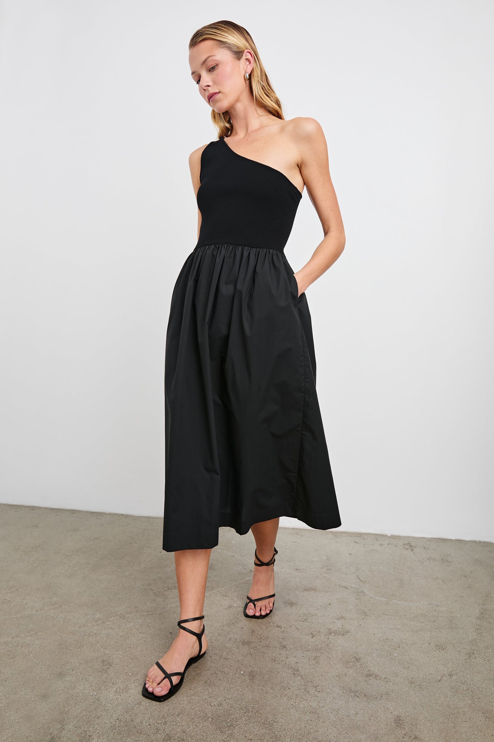 Anita Sleeveless, Midi Dress with an Asymmetrical Neckline and a Cinched Waist in Black Colorway - Front Full Body View Featured on Model