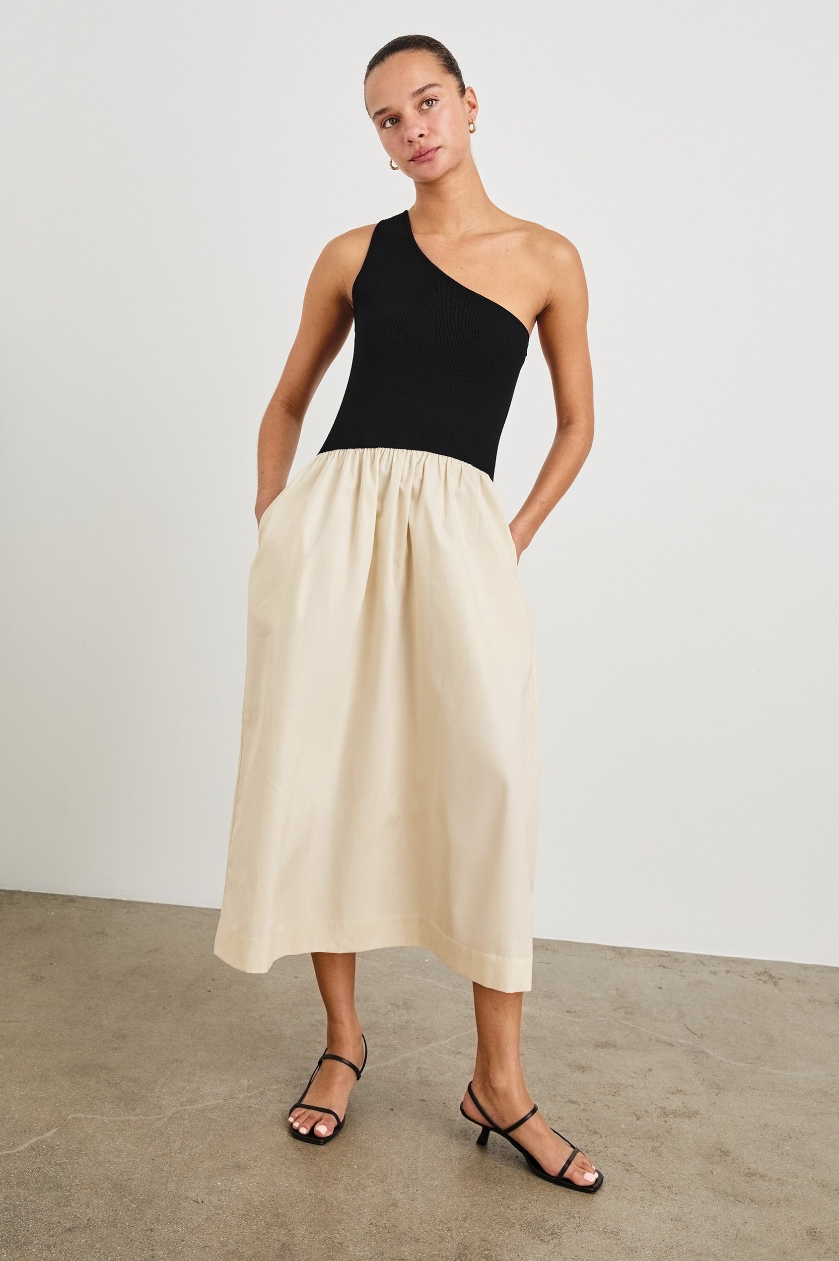 Anita Dress with Black asymmetrical bodice and ivory poplin midi skirt - full front body with hands in pockets, on model