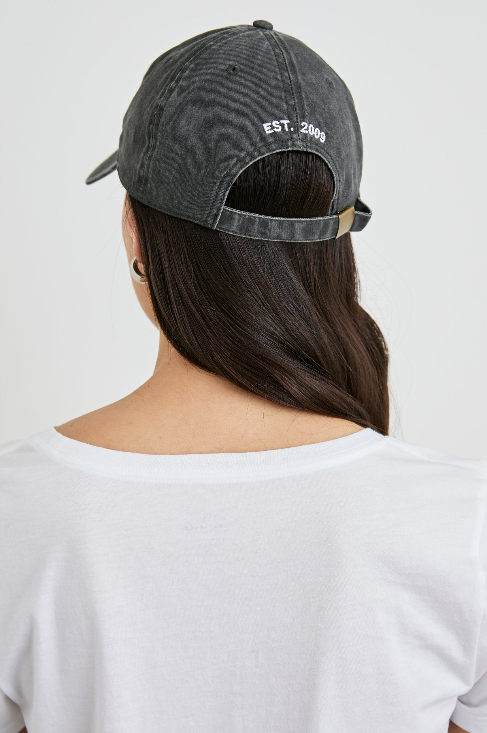 Anniversary Baseball Cap with an Adjustable Back Strap, Front Text, Rails, and Back Text, Est 2009, in Washed Black Colorway, with White Text - Back View Featured on Model