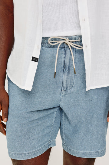 Archer Short in Unlined Cotton Linen With Relaxed Fit, Adjustable Waist Drawstring Ties, Side Pockts, and 8.5-Inch Inseam in Medium Wash Indigo Colorway - Close up View Featured on Model