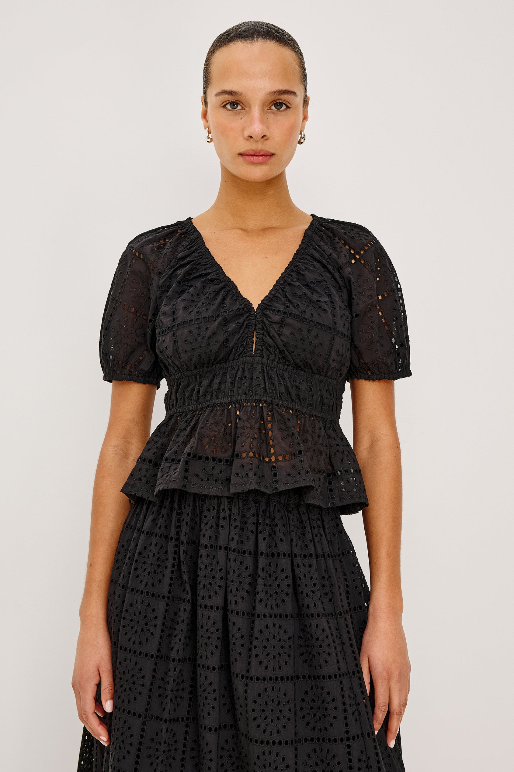 Argenta Top in Cotton Voile With Embroidered Pattern, Short Puff Sleeves, Hook-and-Eye Closure, Elastic V-Neckline and Waist, and Peplum Hem in Black Grid Embroidery Colorway - Upper Body View Featured on Model