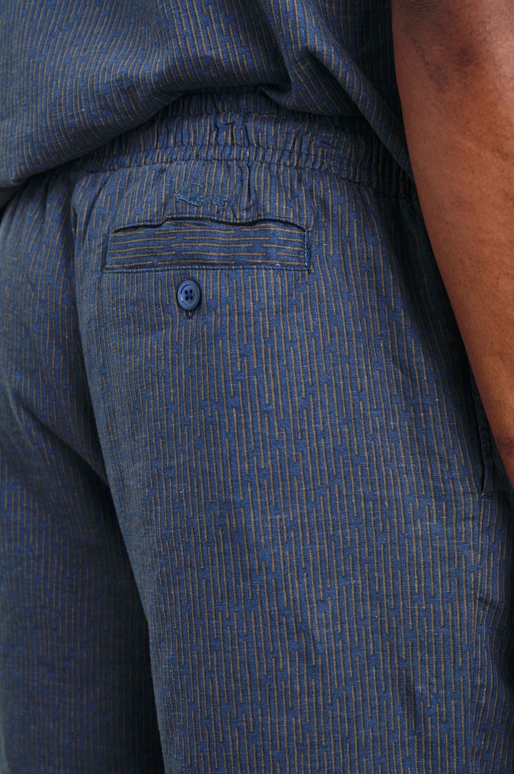 Aries Shorts with a Drawstring Waist, Two Front Pockets and a Buttoned Back Patch Pocket in Navy Cedar Vertical Colorway, with Thin Vertical Cedar Dashes on Navy - Back View Featured on Model