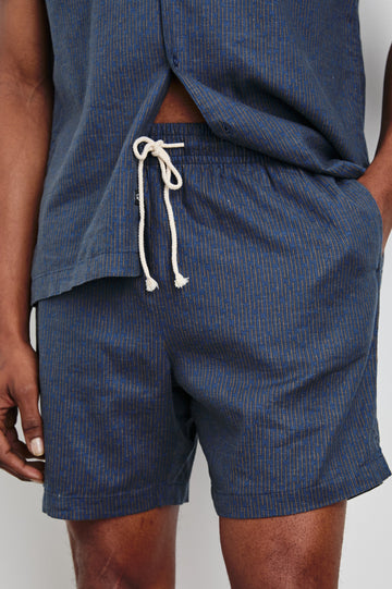 Aries Shorts with a Drawstring Waist, Two Front Pockets and a Buttoned Back Patch Pocket in Navy Cedar Vertical Colorway, with Thin Vertical Cedar Dashes on Navy - Front View Featured on Model
