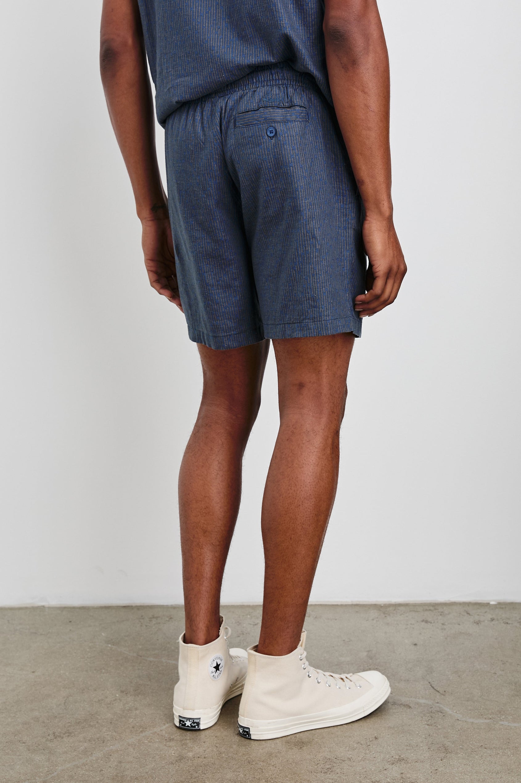 Aries Shorts with a Drawstring Waist, Two Front Pockets and a Buttoned Back Patch Pocket in Navy Cedar Vertical Colorway, with Thin Vertical Cedar Dashes on Navy - Back View Featured on Model