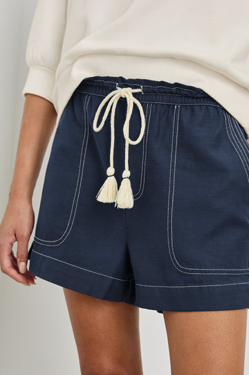 Astra Relaxed Short with an Adjustable Drawcord Waistband and Front Utility Patch Pockets in Navy Colorway with Contrast White Stitching. Front Detailed View Shown on Model.