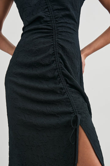 Auren Midi Dress with Cap Sleeves, a Deep V Neck, a Mid-Thigh Side Slit and Ruching from the V Neck to the Slit with a Drawcord at the Slit in Black Jacquard Colorway - Front View Featured on Model 