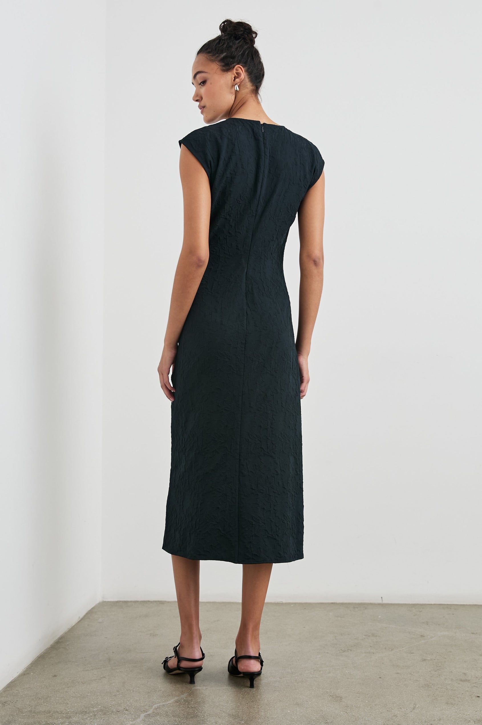 Auren Midi Dress with Cap Sleeves, a Deep V Neck, a Mid-Thigh Side Slit and Ruching from the V Neck to the Slit with a Drawcord at the Slit in Black Jacquard Colorway - Back Full Body View Featured on Model 