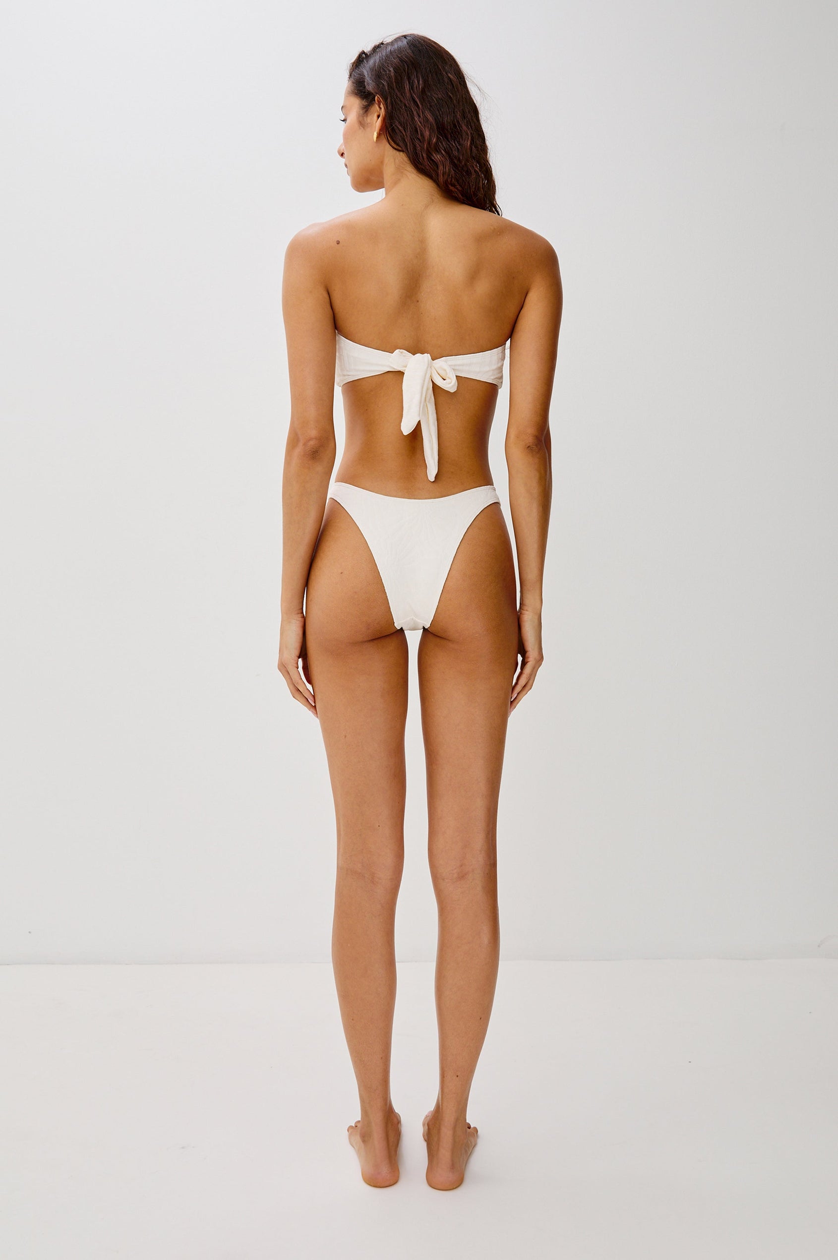 Rocky French Cut Low Rise Bikini Bottom with Spiral Hardware, Fossils Texture and Provides Classic Coverage in Cream Colorway. Full Body Back View Shown on Model.