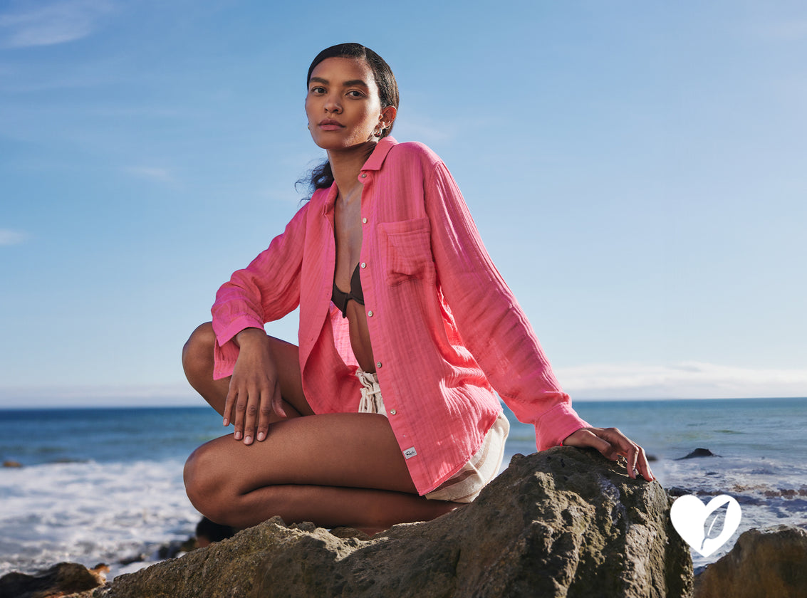 EDITORIAL IMAGE OF MODEL SITTING ON THE BEACH WEARING ELLIS SHIRT IN HIBISCUS AND FOSTER SHORTS IN COCONUT STRIPE