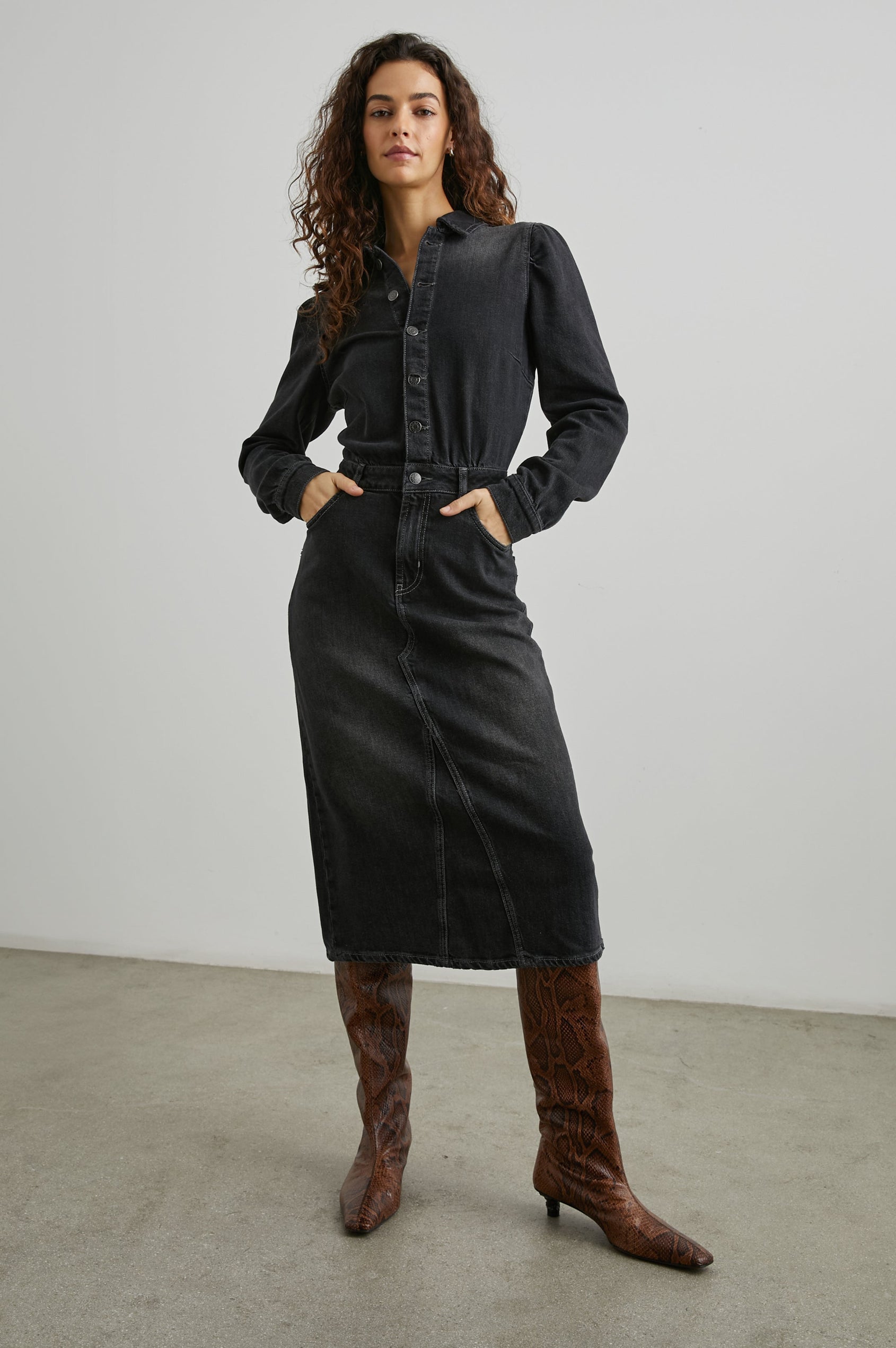 Beverly Long Sleeve Denim Knee Dress with a Back Vent, Belt Loops, a Button and Zipper Closure for the Skirt and Button Closure on the Bodice, a Collar, two Front Pockets plus a Coin Pocket and Two Back Patch Pockets in Eclipse Colorway, a Black - Front Full Body View Featured on Model