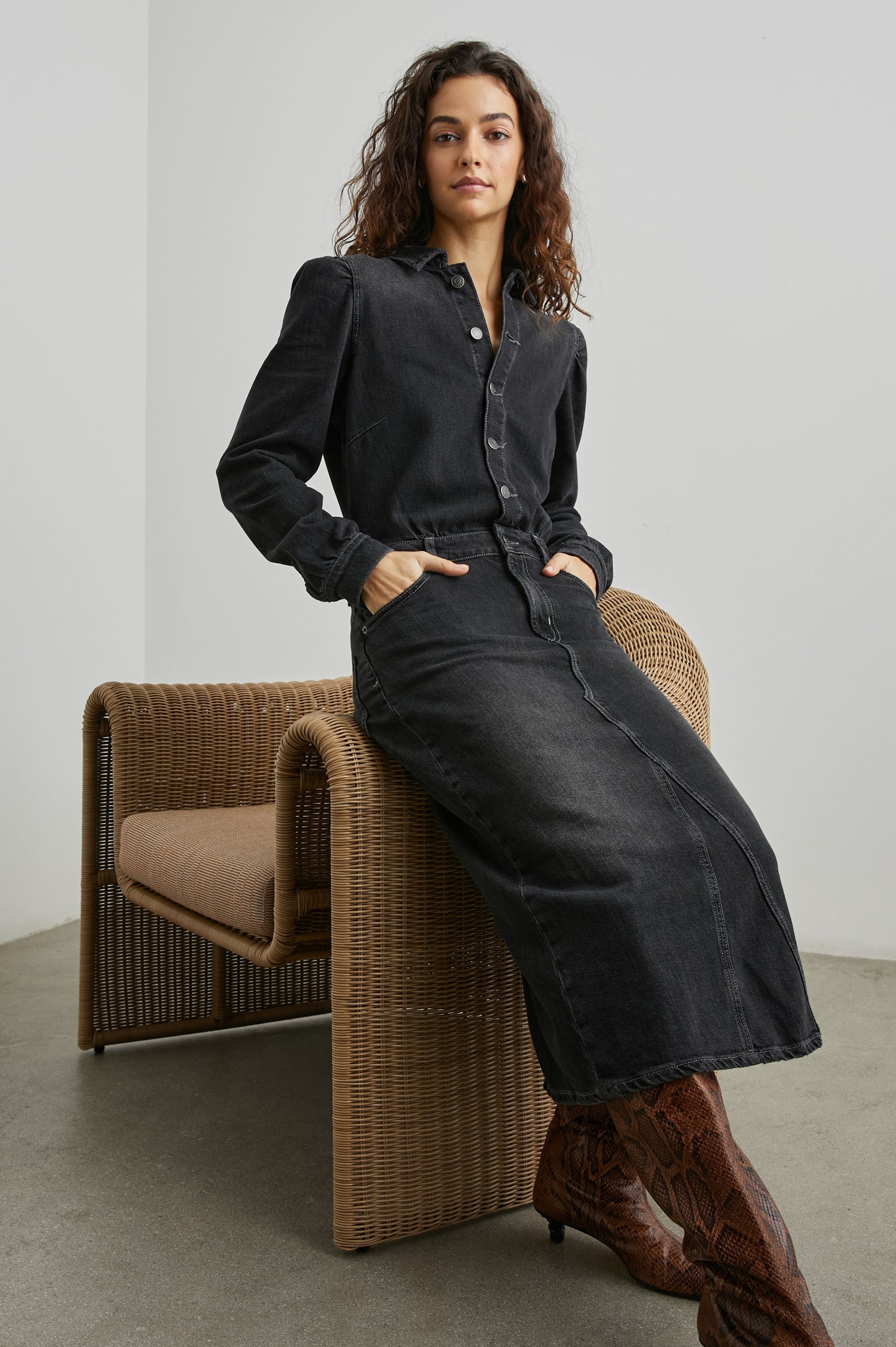 Beverly Long Sleeve Denim Knee Dress with a Back Vent, Belt Loops, a Button and Zipper Closure for the Skirt and Button Closure on the Bodice, a Collar, two Front Pockets plus a Coin Pocket and Two Back Patch Pockets in Eclipse Colorway, a Black - Front Full Body View Featured on Seated Model