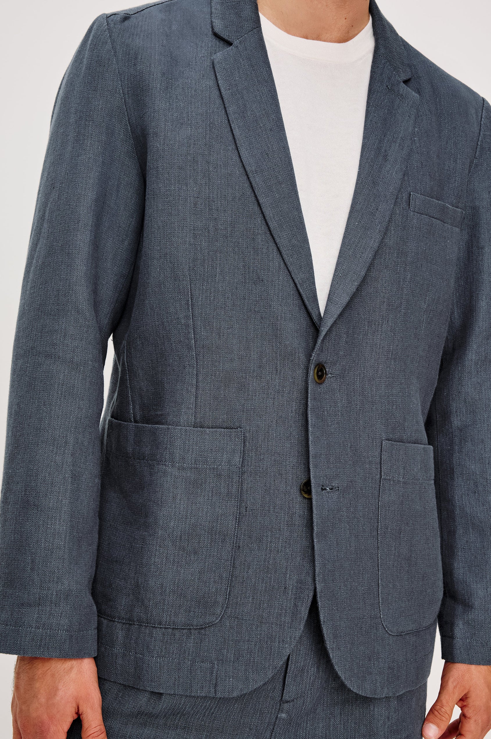 The Bond is a single breasted blazer with two buttons, one chest pocket and two patch pockets in a blue Meridian colorway. Front detail view featured on model.