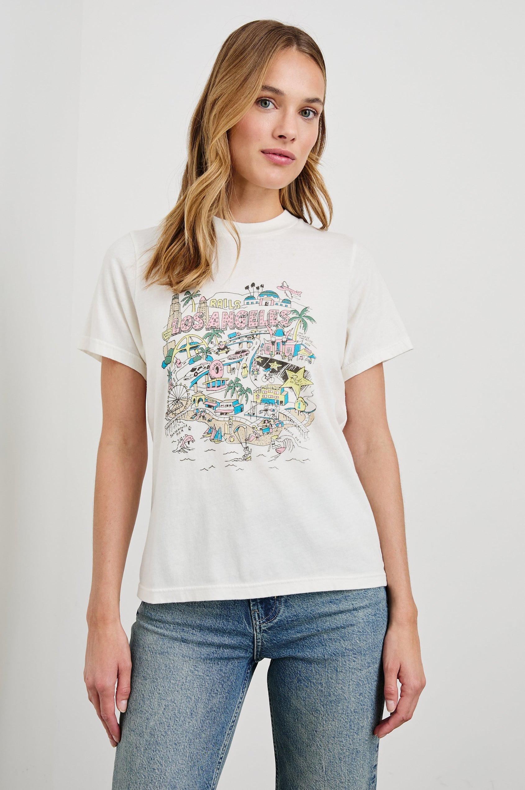 Boyfriend T-Shirt with a Crew Neck, an image of Los Angeles sites and objects, and the text, Rails Los Angeles in Rails Los Angeles Map White Colorway, with text and image in yellow, pink, blue and tan - Front View Featured on Model