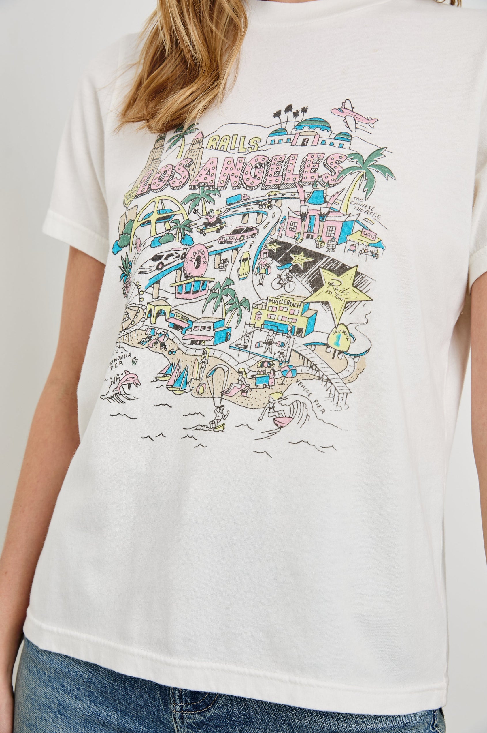 Boyfriend T-Shirt with a Crew Neck, an image of Los Angeles sites and objects, and the text, Rails Los Angeles in Rails Los Angeles Map White Colorway, with text and image in yellow, pink, blue and tan - Front View Featured on Model