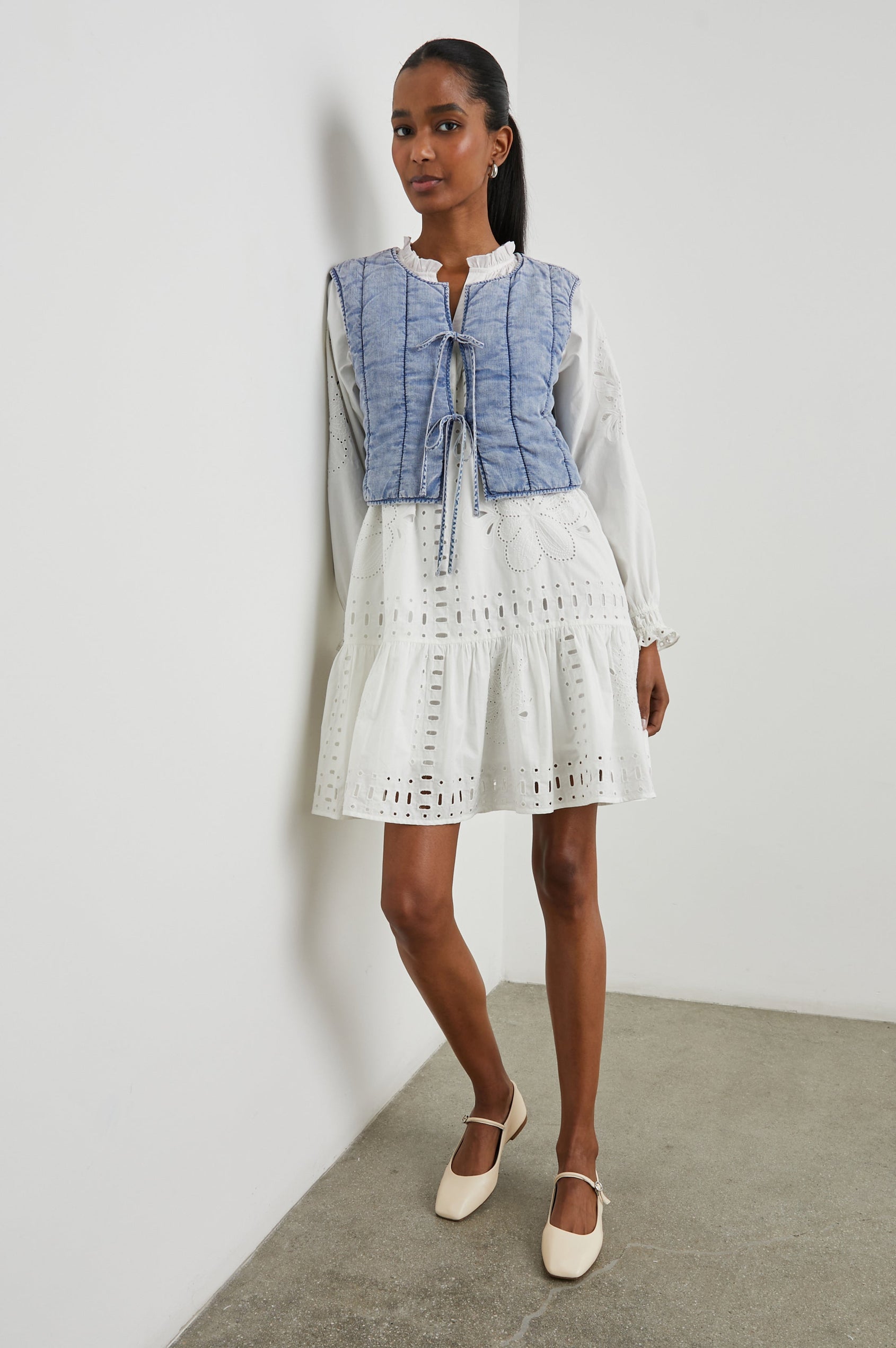 Bronte Sleeveless Cropped Denim Top with Front Tie Closure and Vertical Seams in Medium Cloud Wash Colorway - Front Full Body View Featured on Model, Layered Over a Second Shirt 