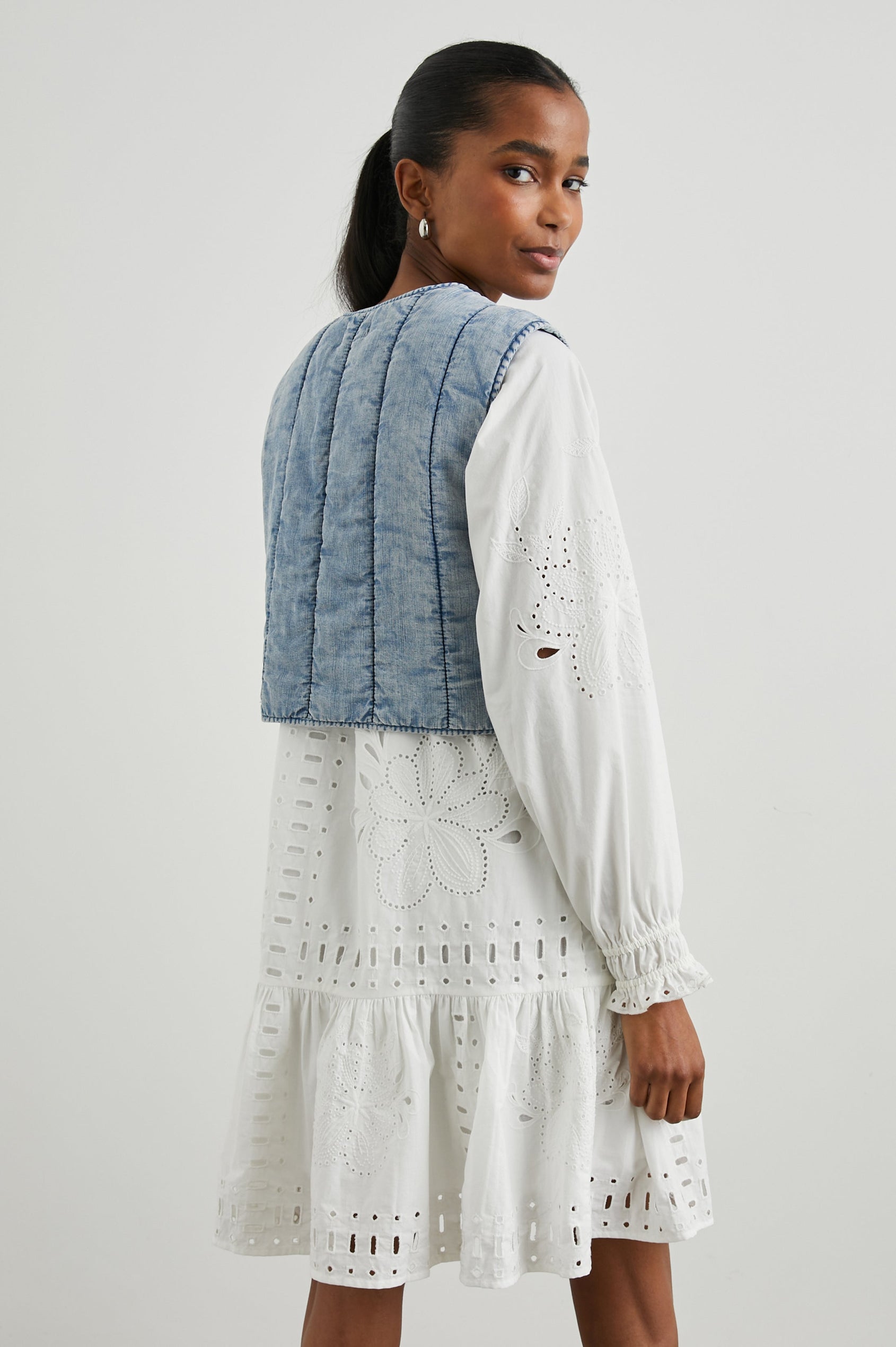 Bronte Sleeveless Cropped Denim Top with Front Tie Closure and Vertical Seams in Medium Cloud Wash Colorway - Back View Featured on Model, Layered Over a Second Shirt 