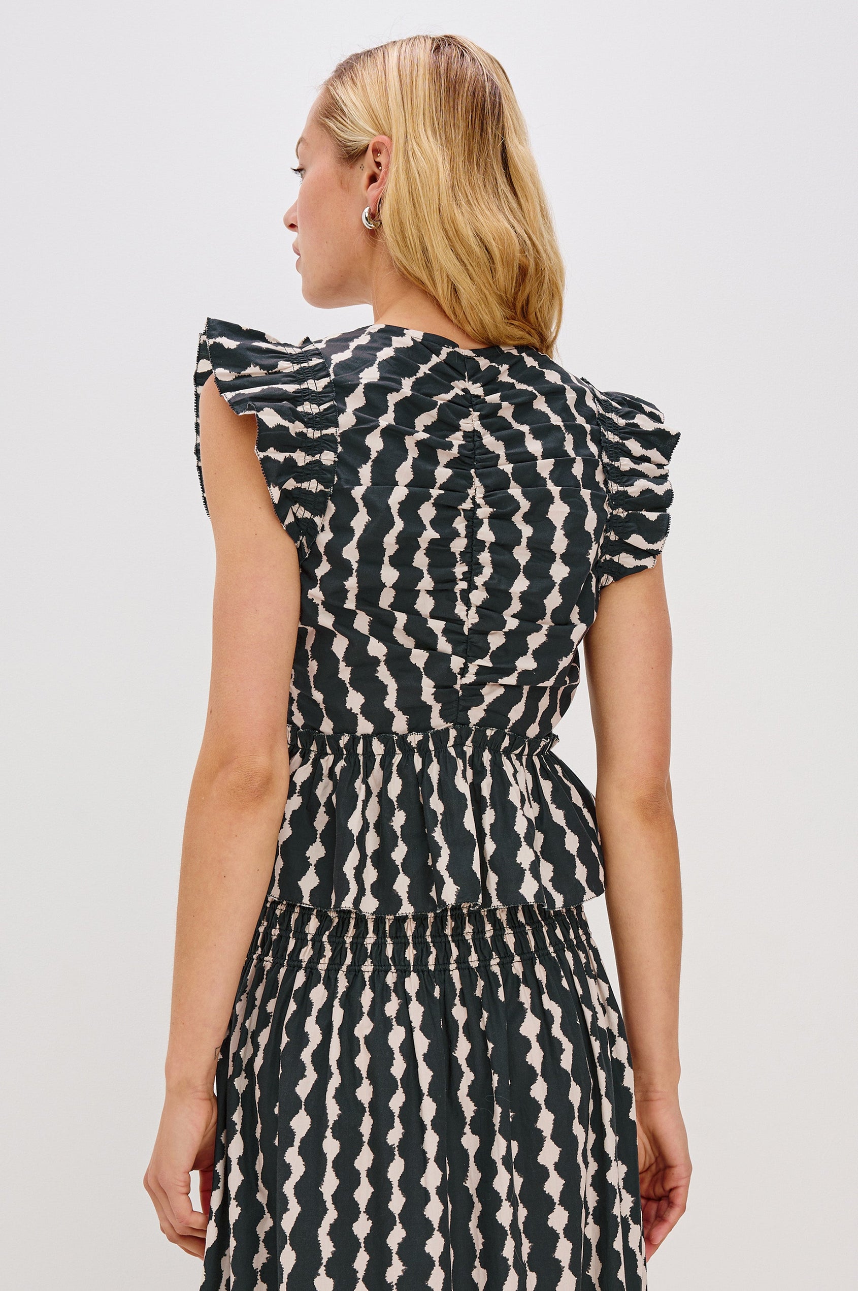 Cali short sleeve top with center front ruching, flutter sleeves, and a ruffle hem in Painted Noir colorway - back view on model