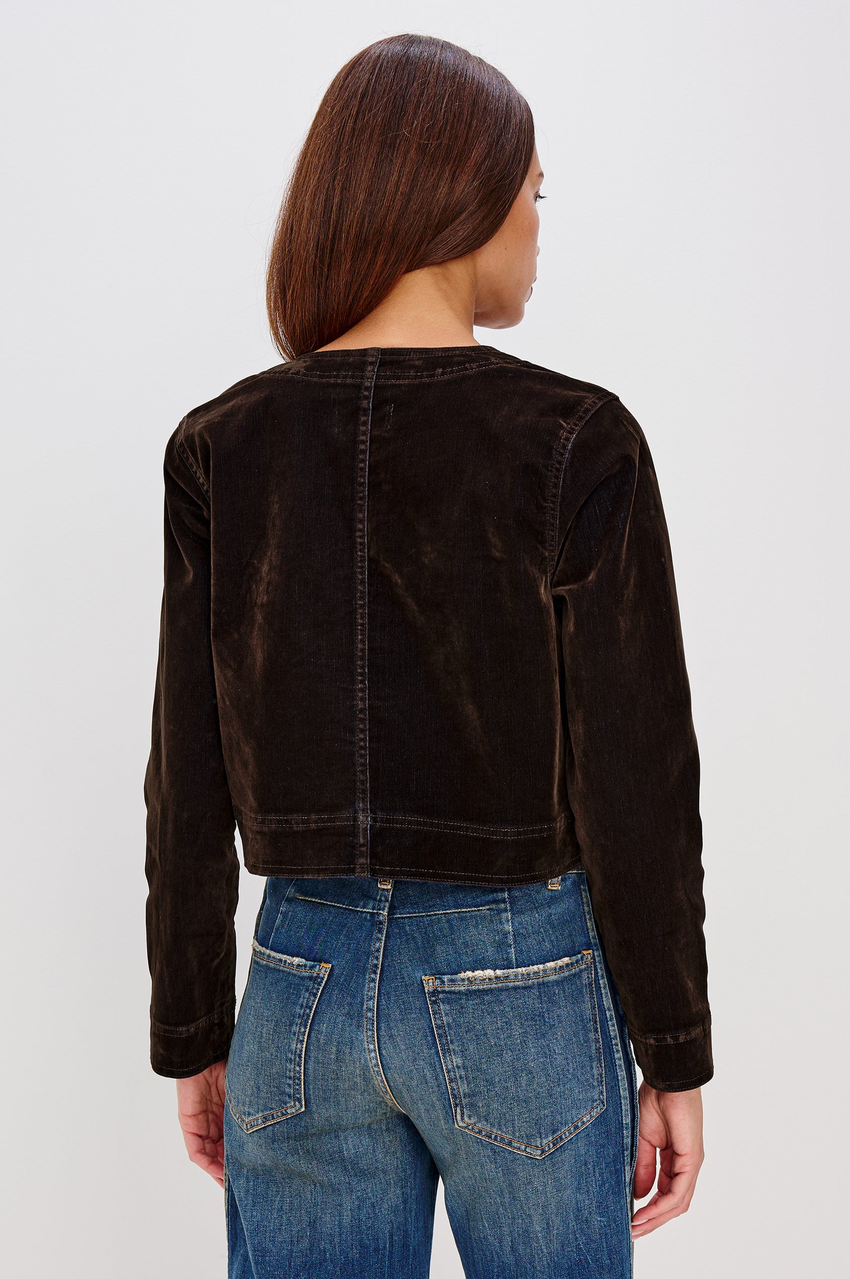 The Capistrano is a cropped denim jacket with a crewneck, it has a button front and two chest pockets in Chocolate Flocking colorway. Back view featured on model.