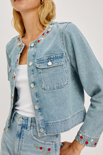 Capistrano Lady Jacket in Recycled Cotton Denim Blend With Floral Embroidery, Chest Flap Buttoned Pockets, and Long Sleeves in Dainty Rose Colorway - Upper Body Close Up View Featured on Model