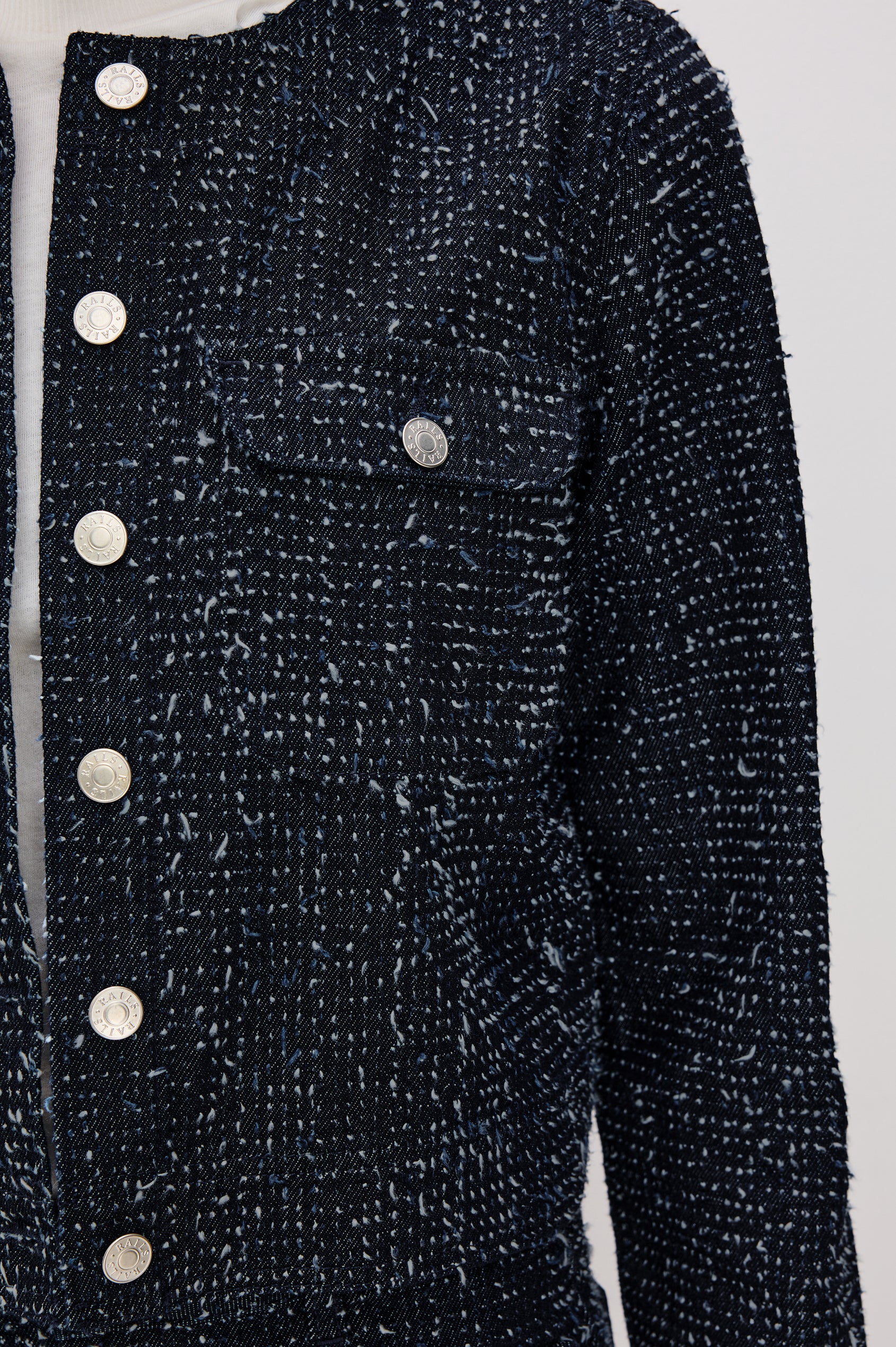 The Capistrano is a cropped denim jacket with a crewneck, it has a button front and two chest pockets in Denim Tweed colorway. Front detail view featured on model.