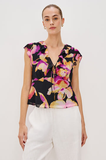 Carmine blouse, a chiffon top with ruffled cap sleeves, ruffles at the v-neckline, a front tie, and empire waist silhouette in Dusk Orchid Colorway. Front View Shown on Model.