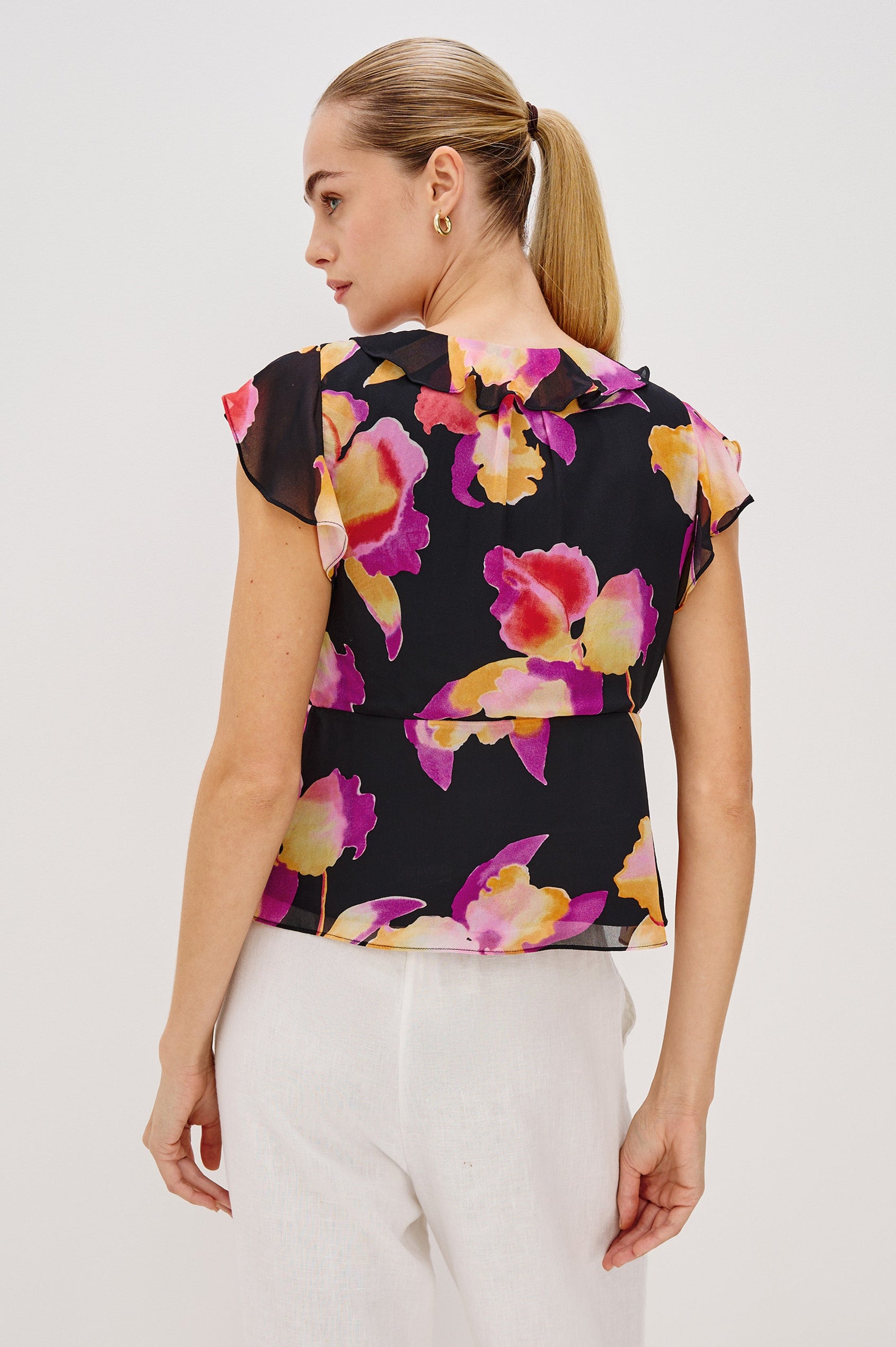 Carmine blouse, a chiffon top with ruffled cap sleeves, ruffles at the v-neckline, a front tie, and empire waist silhouette in Dusk Orchid Colorway. Back View Shown on Model.