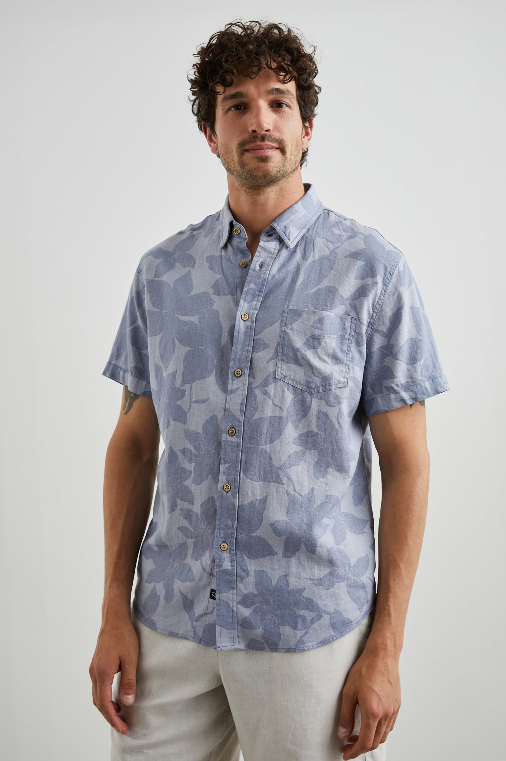 Carson Short Sleeve Button Up with a Chest Patch Pocket in Garden Sands Orchid Colorway, Blue Flowers on Light Blue - Front View Featured on Model
