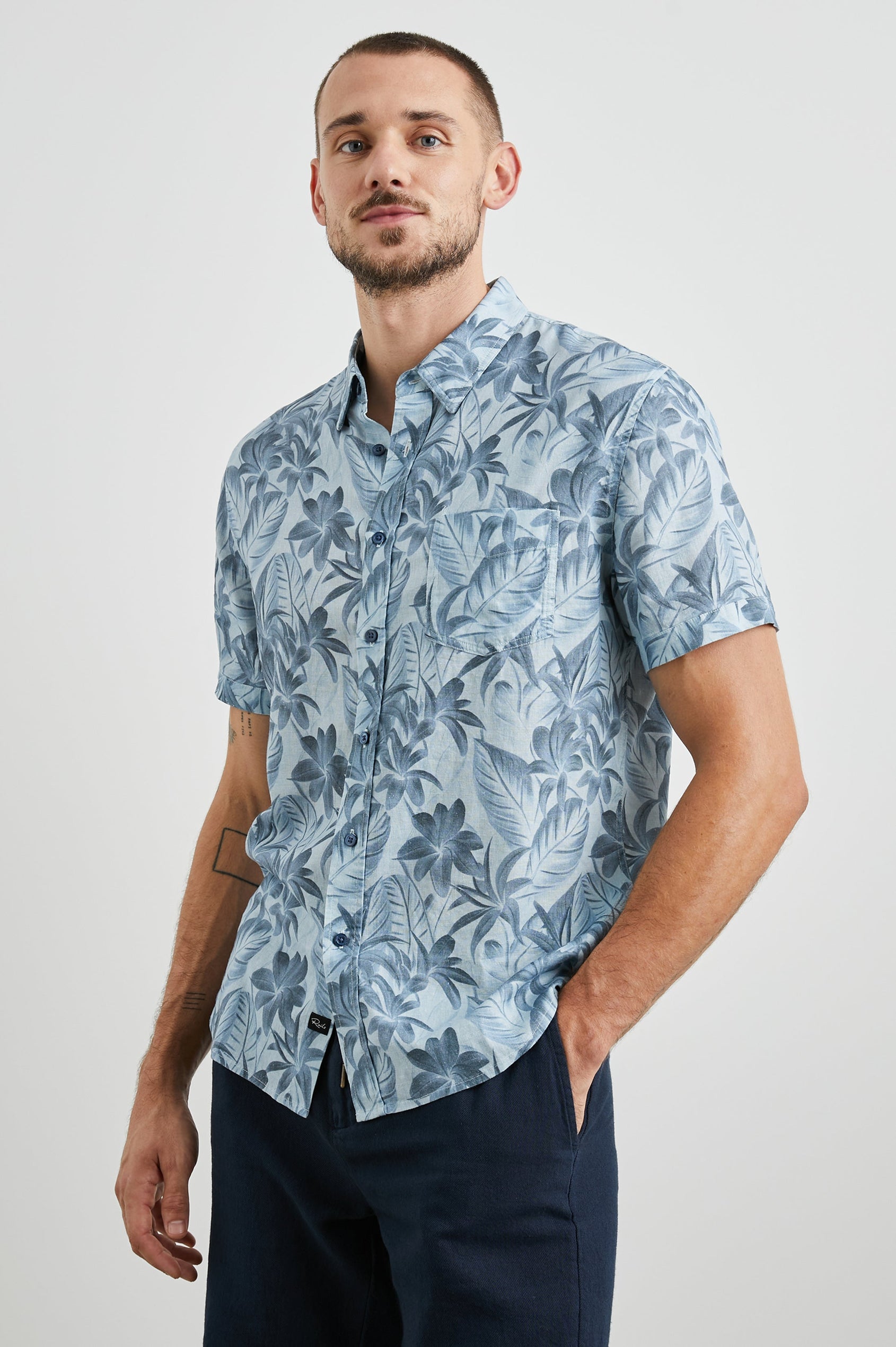 Carson Short Sleeve Button Up with a Chest Patch Pocket in Jungle Garden Reflection Colorway, Flowers and Leaves in Blues on Light Blue - Front View Featured on Model