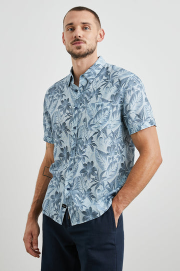 Carson Short Sleeve Button Up with a Chest Patch Pocket in Jungle Garden Reflection Colorway, Flowers and Leaves in Blues on Light Blue - Front View Featured on Model