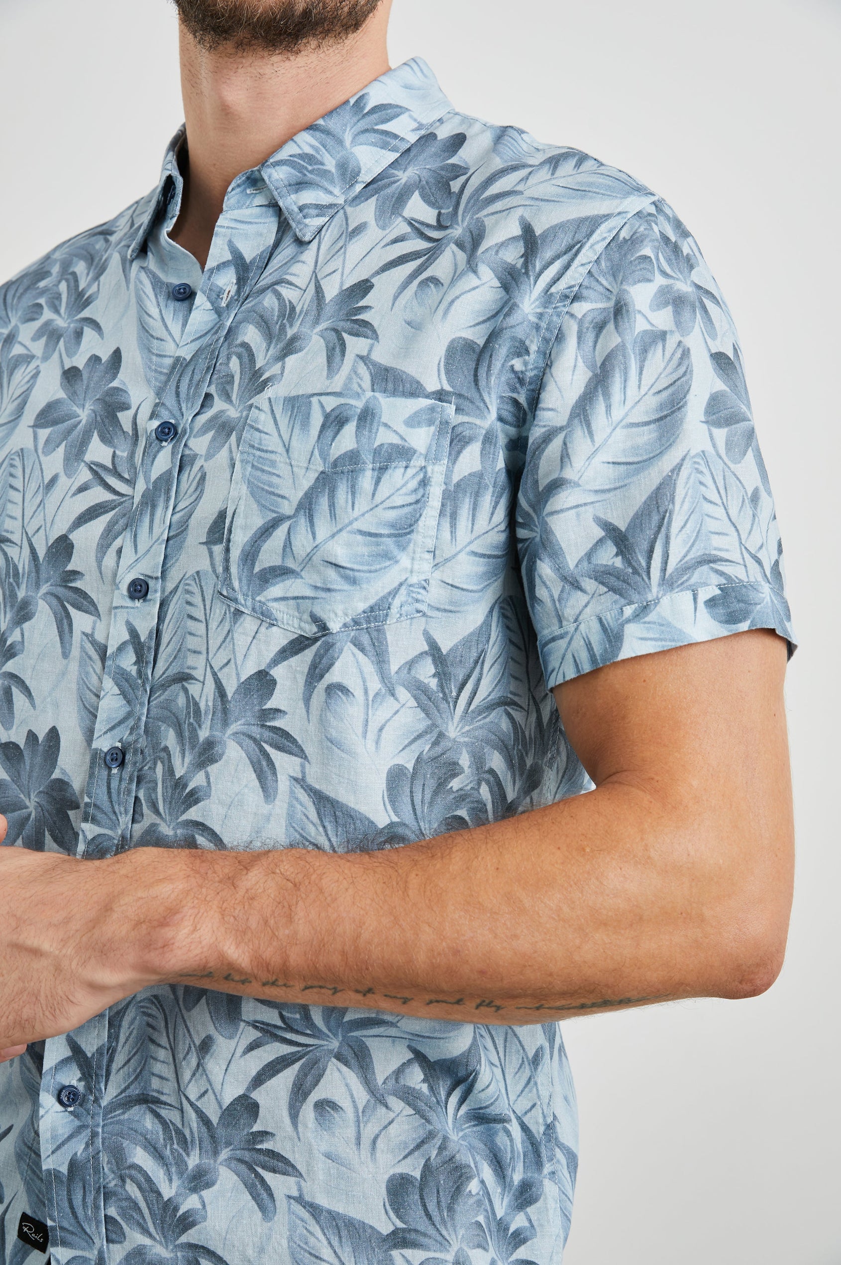 Carson Short Sleeve Button Up with a Chest Patch Pocket in Jungle Garden Reflection Colorway, Flowers and Leaves in Blues on Light Blue - Front View Featured on Model