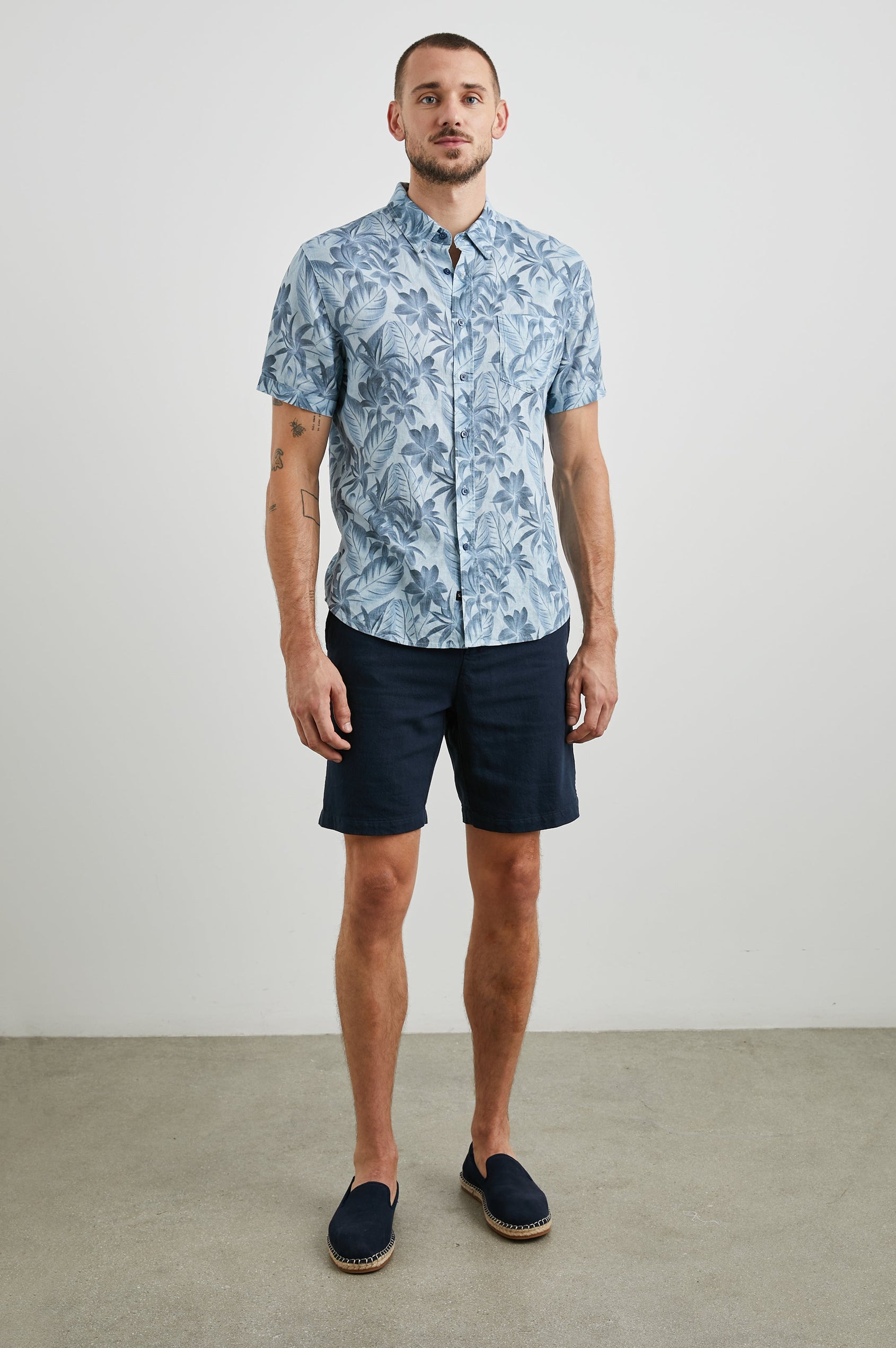 Carson Short Sleeve Button Up with a Chest Patch Pocket in Jungle Garden Reflection Colorway, Flowers and Leaves in Blues on Light Blue - Front Full Body View Featured on Model