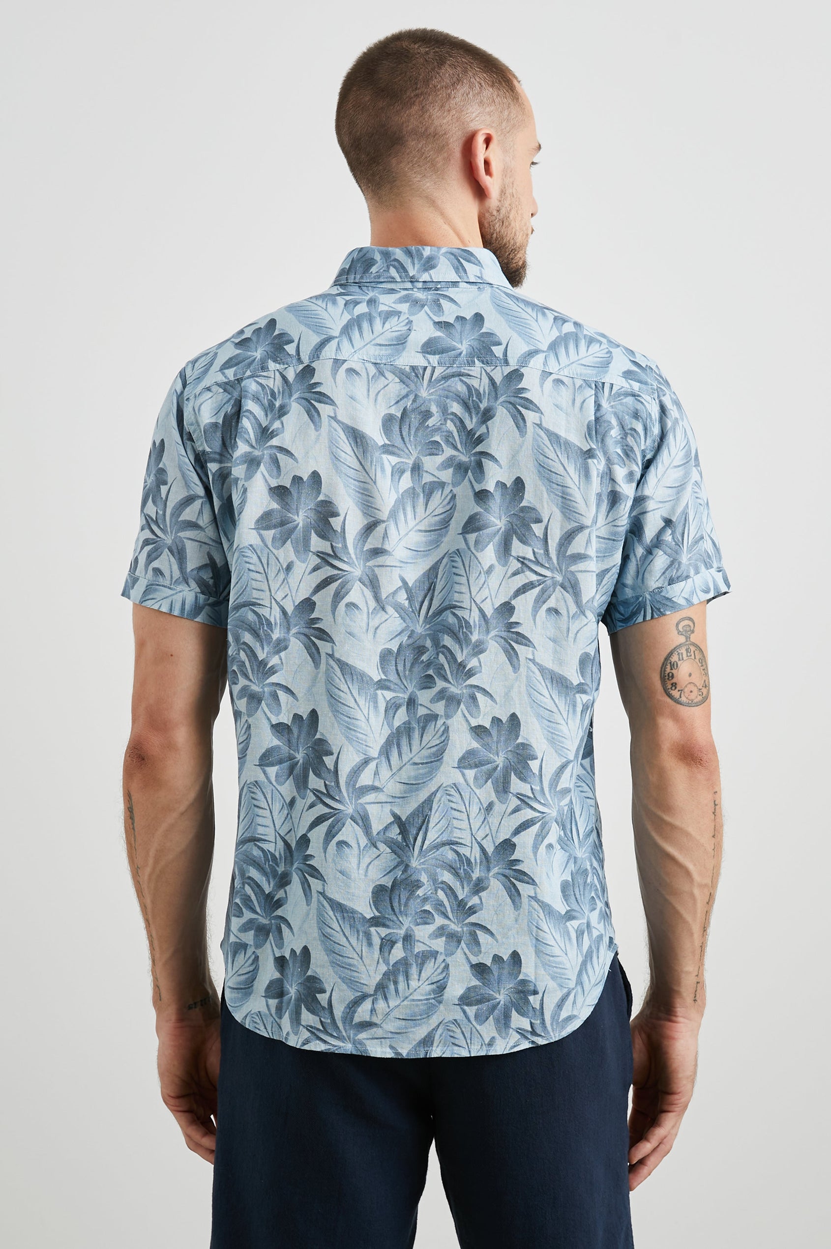 Carson Short Sleeve Button Up with a Chest Patch Pocket in Jungle Garden Reflection Colorway, Flowers and Leaves in Blues on Light Blue - Back View Featured on Model