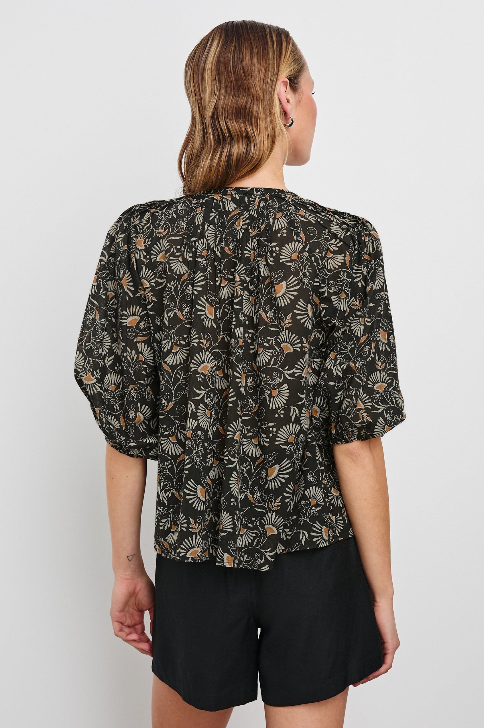 Cassat Blouse with a Deep V-Neckline, Mid-Length Sleeves with Elastic Openings in Cassia Colorway, with white and orange flowers on black - Back Untucked View Featured on Model