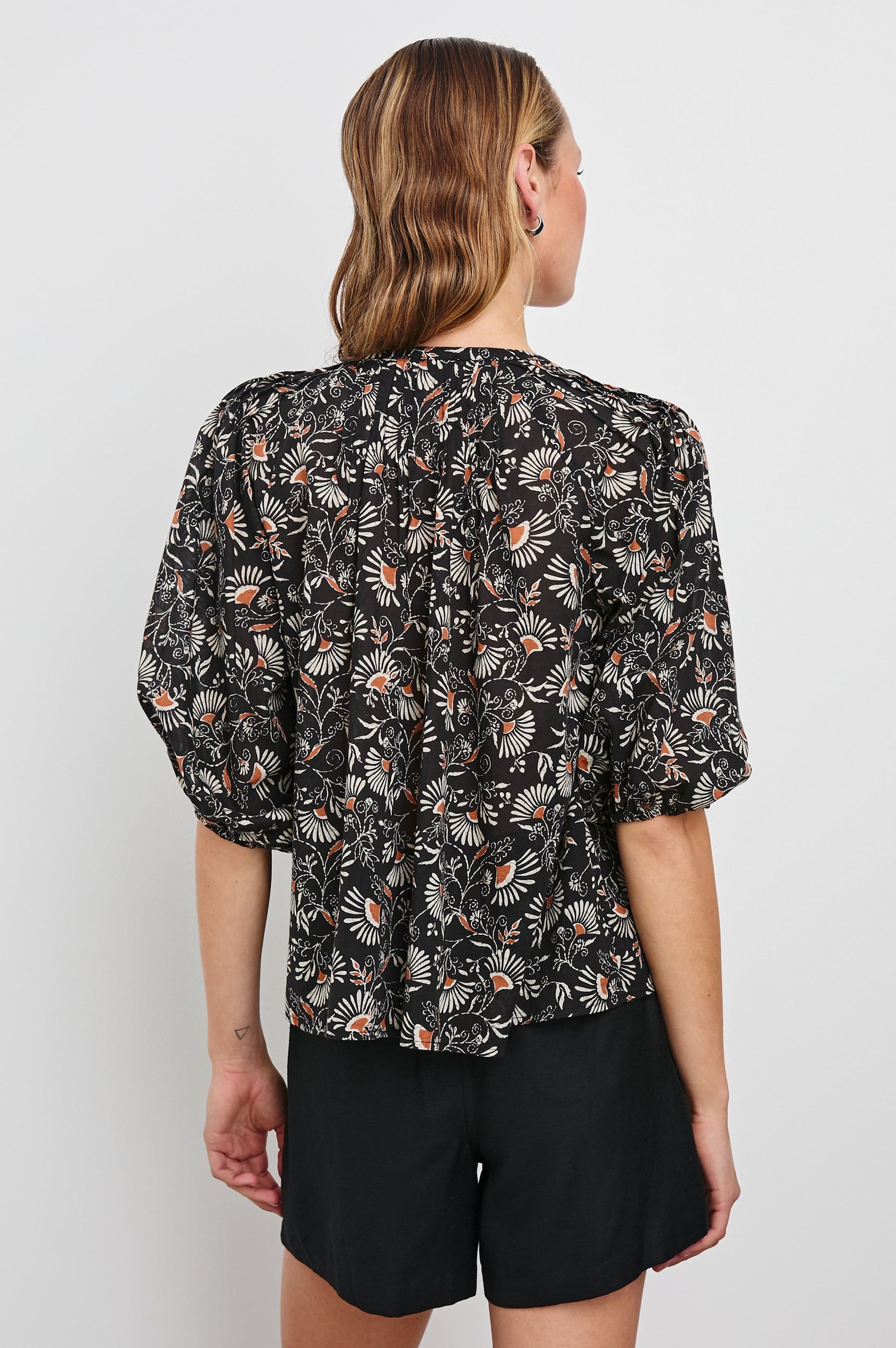 Cassat Blouse with a Deep V-Neckline, Mid-Length Sleeves with Elastic Openings in Cassia Colorway, with white and orange flowers on black - Back Untucked View Featured on Model