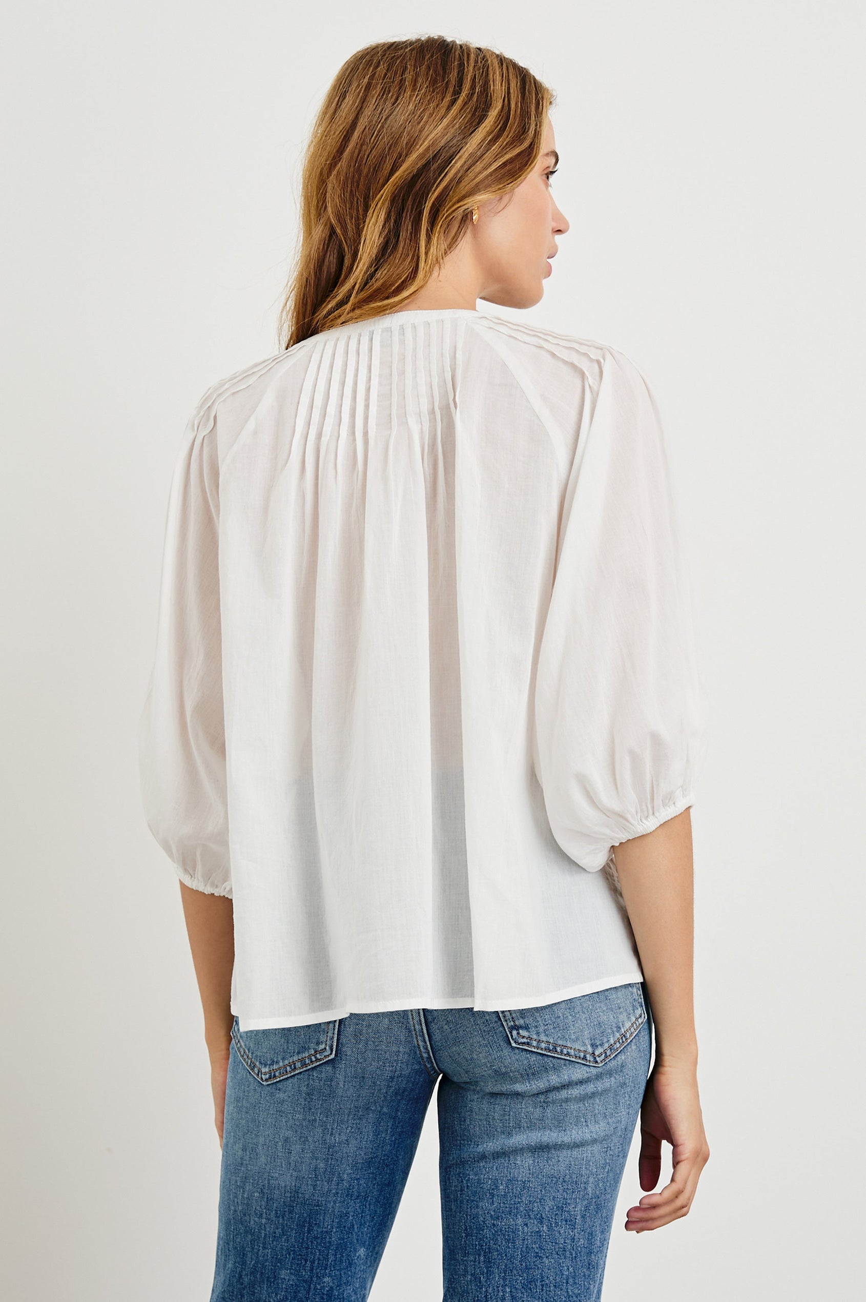 Cassat Blouse with a Deep V-Neckline, Mid-Length Sleeves with Elastic Openings and Pleating around Neckline in White Colorway - Back Untucked View Featured on Model