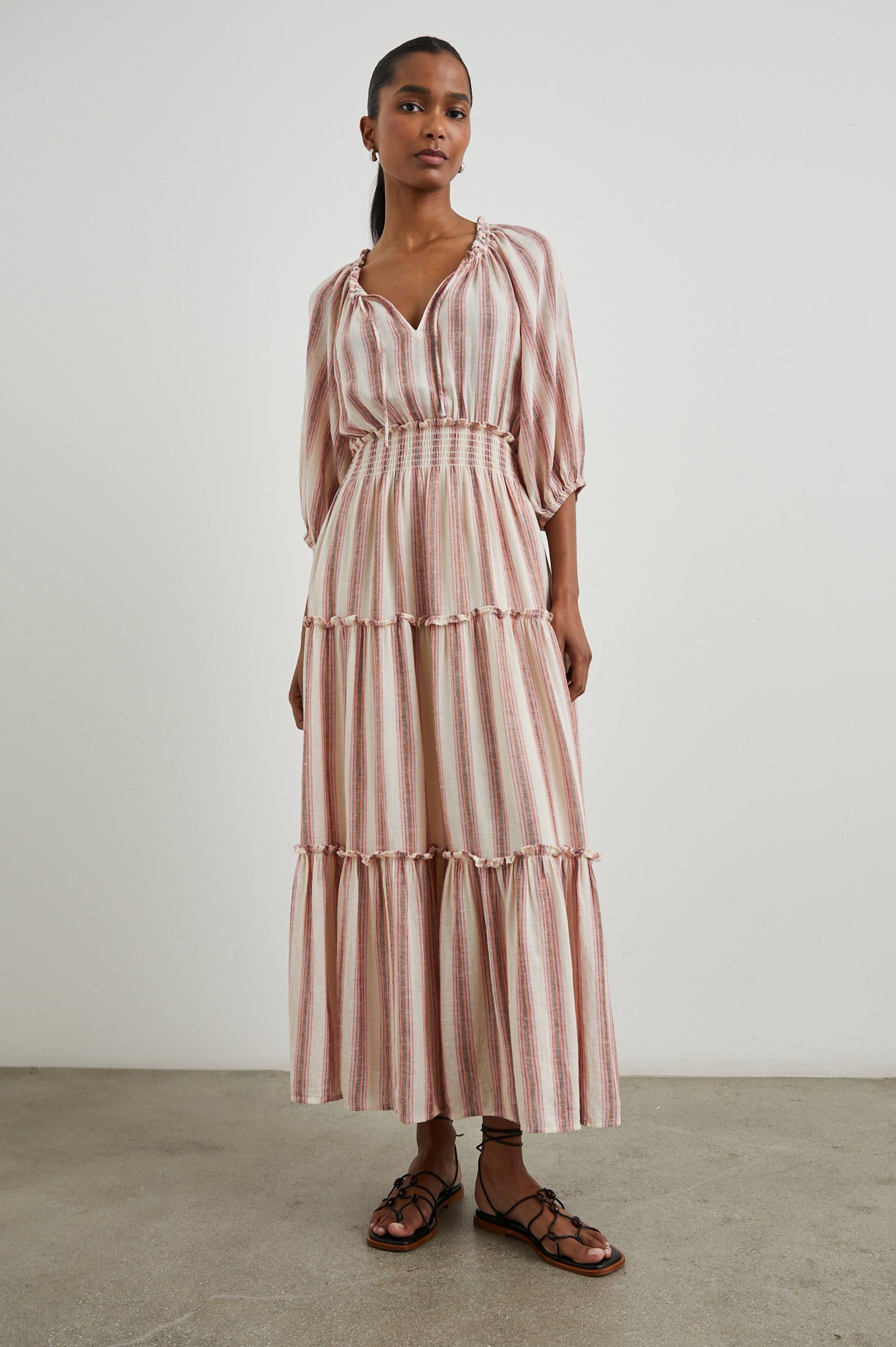 Caterine Maxi Dress with Mid-length Sleeves, a V neck, a Shirred Collar with a tie, a Smocked Waist, and a Tiered Skirt in Camino Stripe Colorway, a vertical stripe with cream, grey, purple and orange  - Front Full Body View Featured on Model