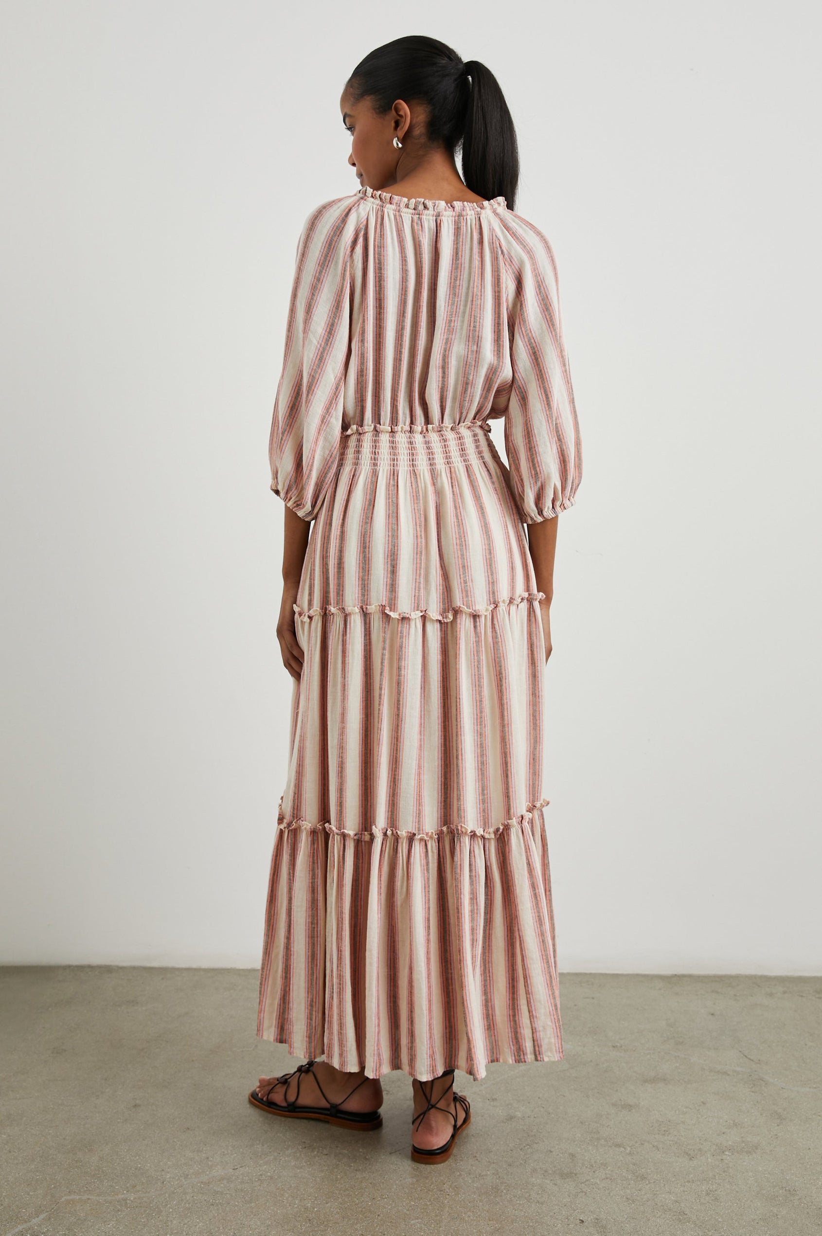 Caterine Maxi Dress with Mid-length Sleeves, a V neck, a Shirred Collar with a tie, a Smocked Waist, and a Tiered Skirt in Camino Stripe Colorway, a vertical stripe with cream, grey, purple and orange  - Back Full Body View Featured on Model