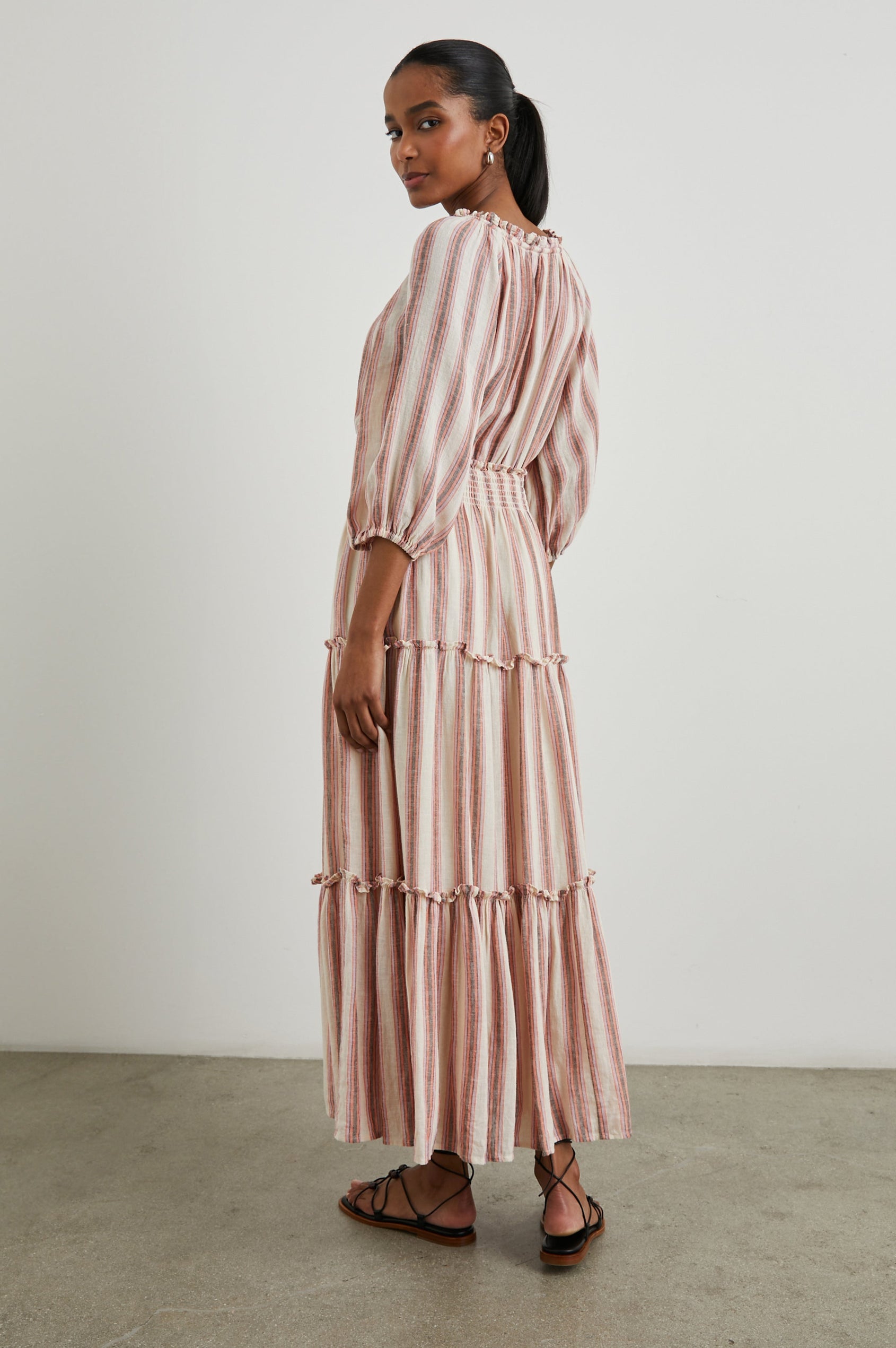 Caterine Maxi Dress with Mid-length Sleeves, a V neck, a Shirred Collar with a tie, a Smocked Waist, and a Tiered Skirt in Camino Stripe Colorway, a vertical stripe with cream, grey, purple and orange  - Back Full Body View Featured on Model